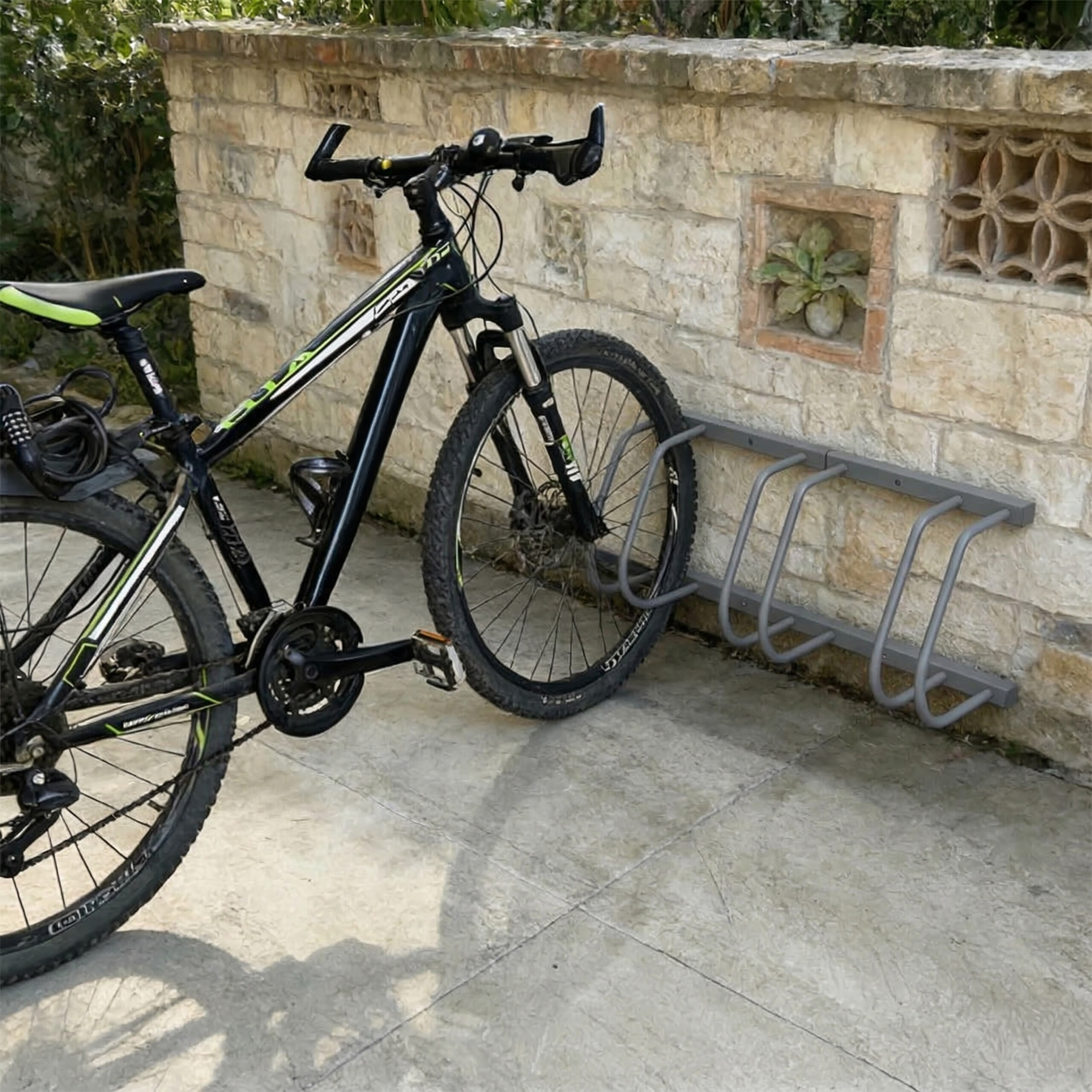 Ein schwarzes Mountainbike geparkt in einem Metallständer vor einer rustikalen Steinwand.