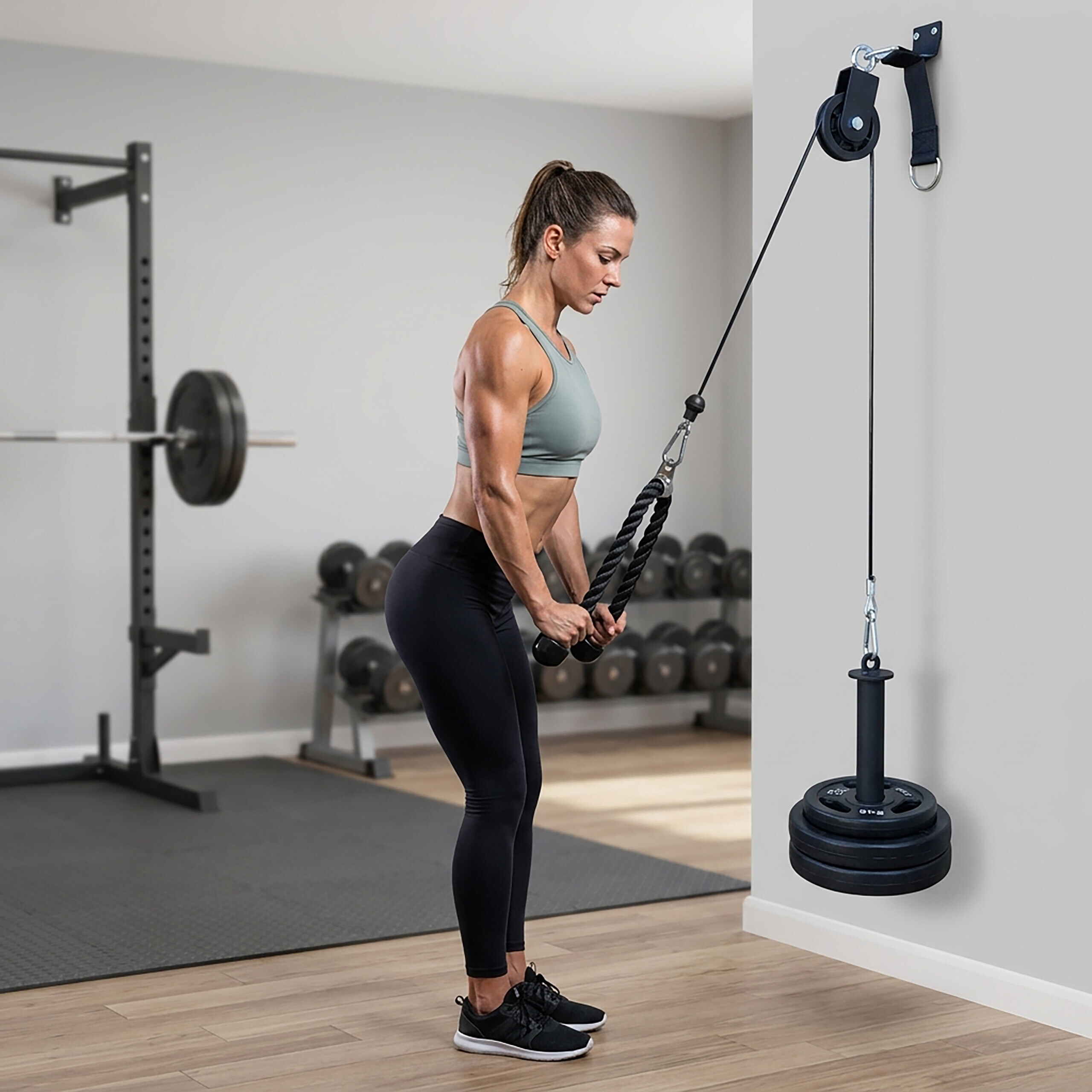 Eine Frau in Sportkleidung trainiert im Fitnessstudio an einem Wandkabelzug mit Zusatzgewichten.