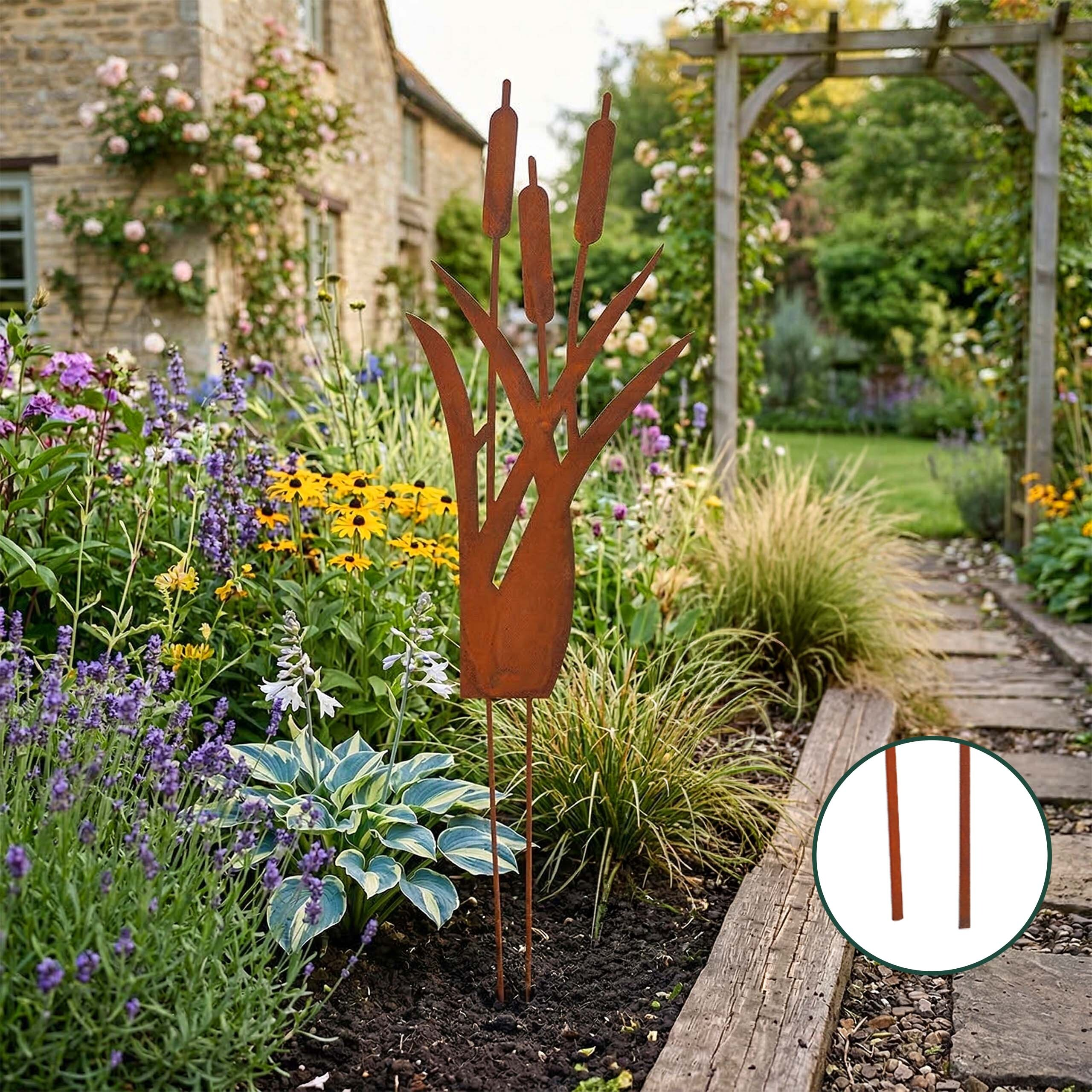 Rostiger Metall-Rohrkolben-Gartenstecker in einem üppigen Blumenbeet mit bunten Pflanzen und Steinweg.