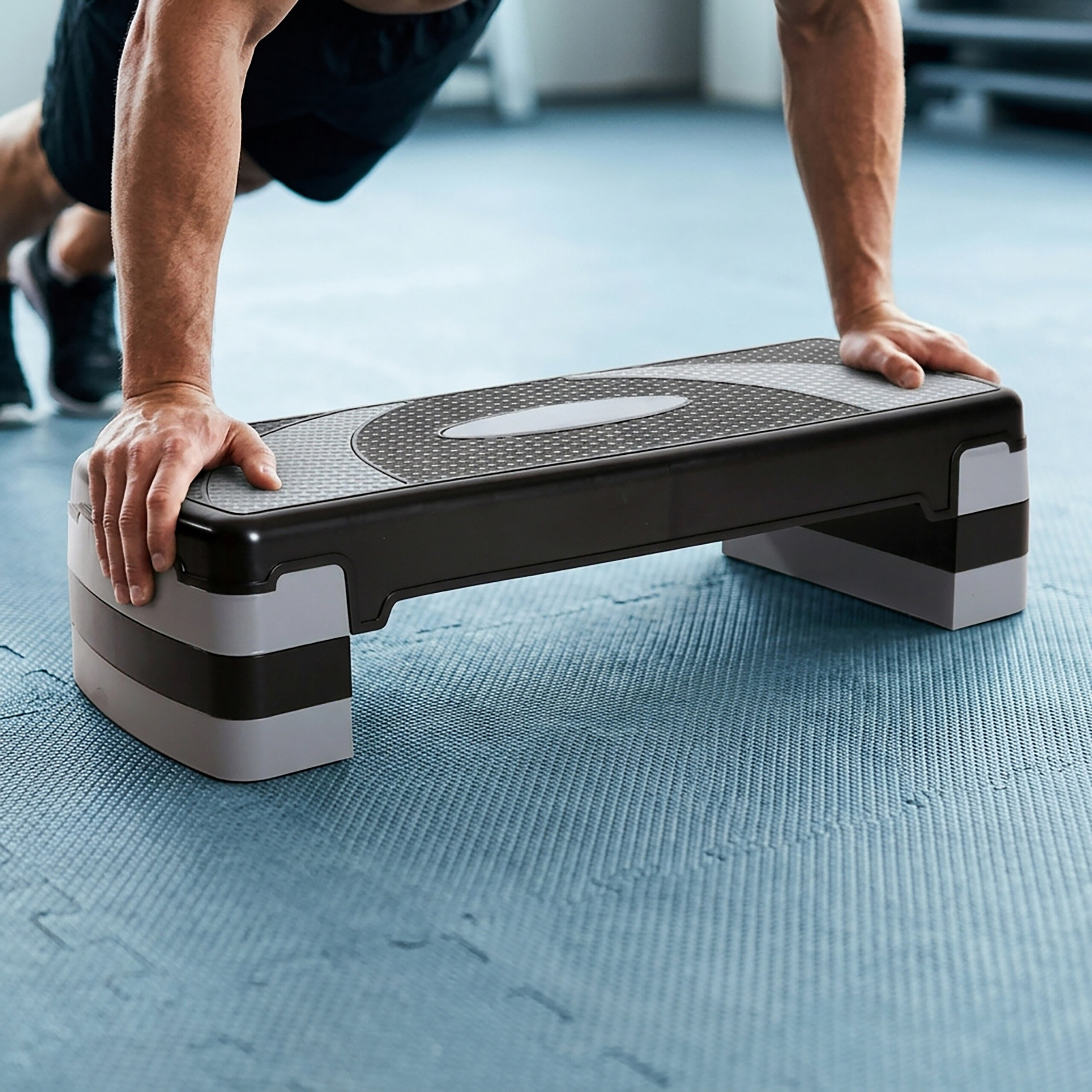 Ein Mann macht Liegestütze auf einem schwarzen Stepper in einem Fitnessstudio.