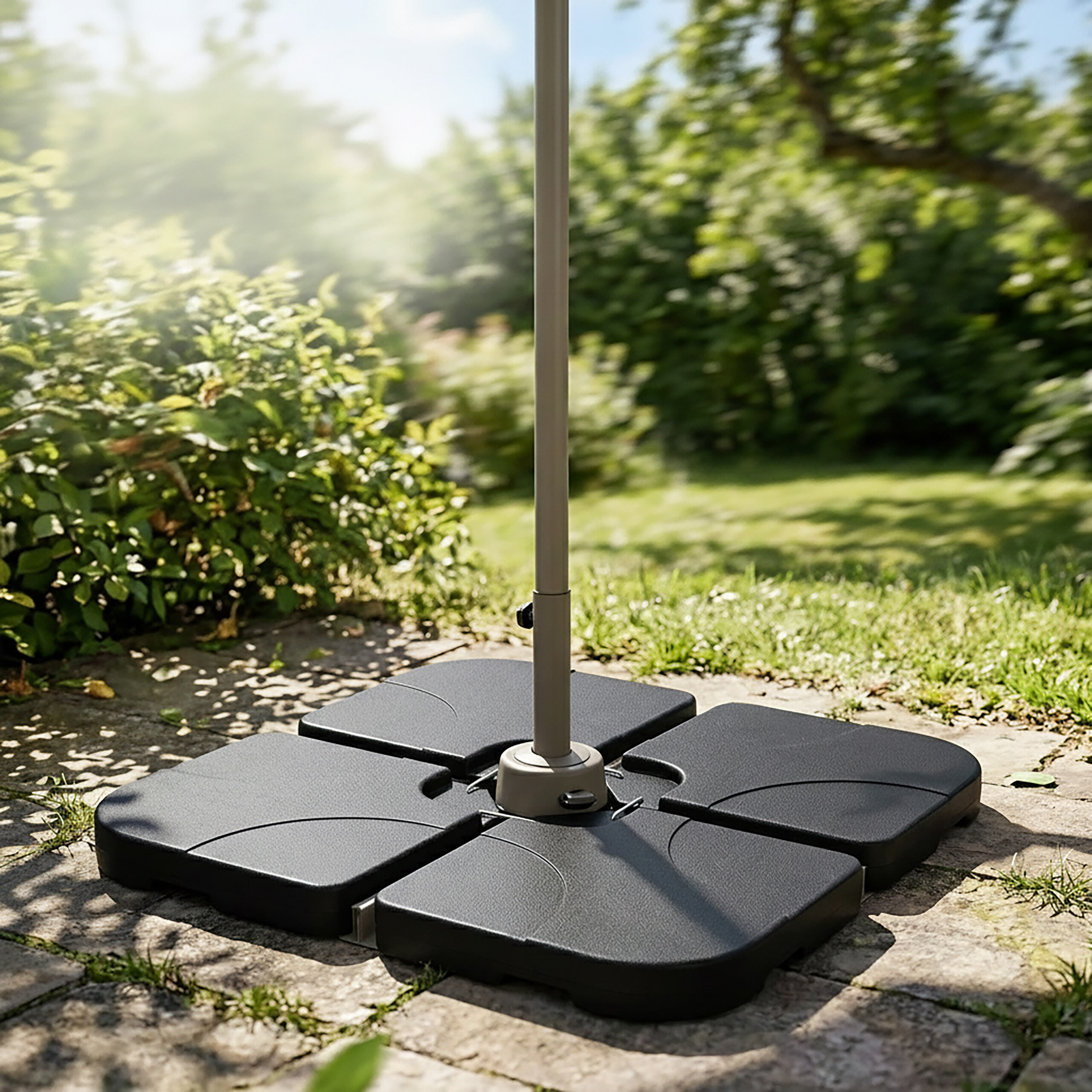 Ein grauer Sonnenschirmständer aus vier schwarzen Platten steht auf einer Steinterrasse in einem Garten.