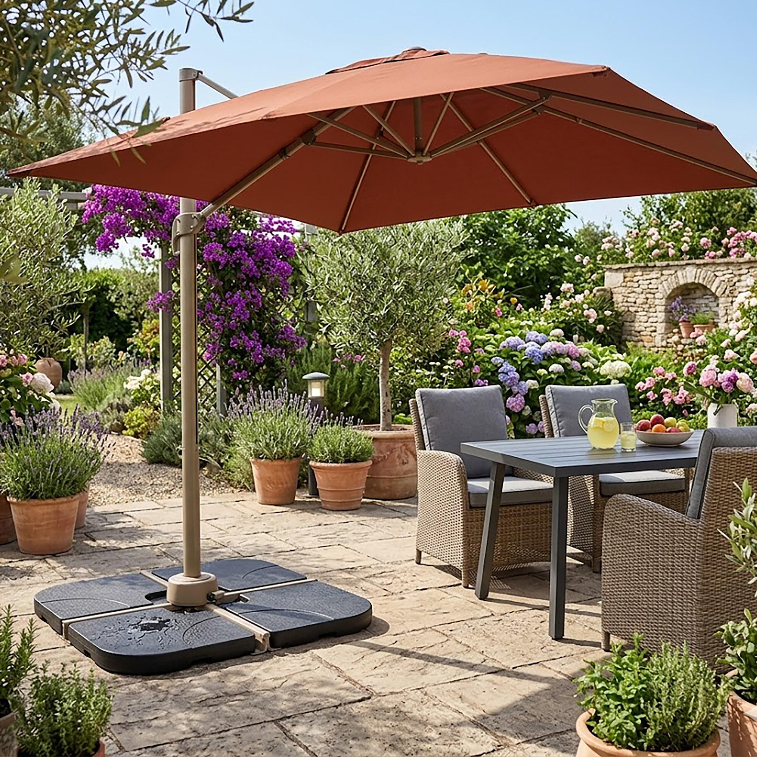 Ein großer rostterrakottafarbener Sonnenschirm steht über einem Tisch und Korbstühlen auf einer sonnigen Gartenterrasse.