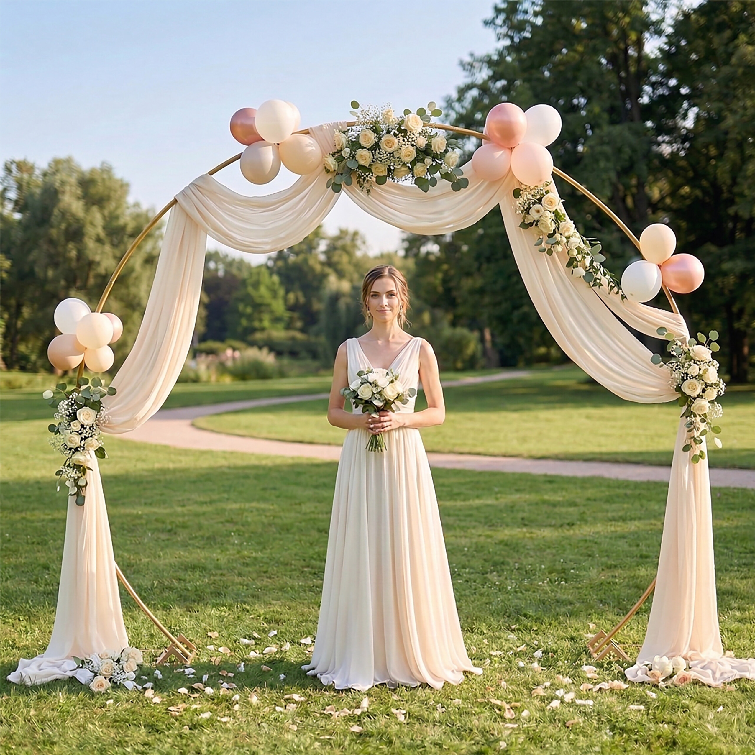 Eine Braut im langen weißen Kleid steht unter einem Hochzeitsbogen aus Blumen, Ballons und Stoff im Park.