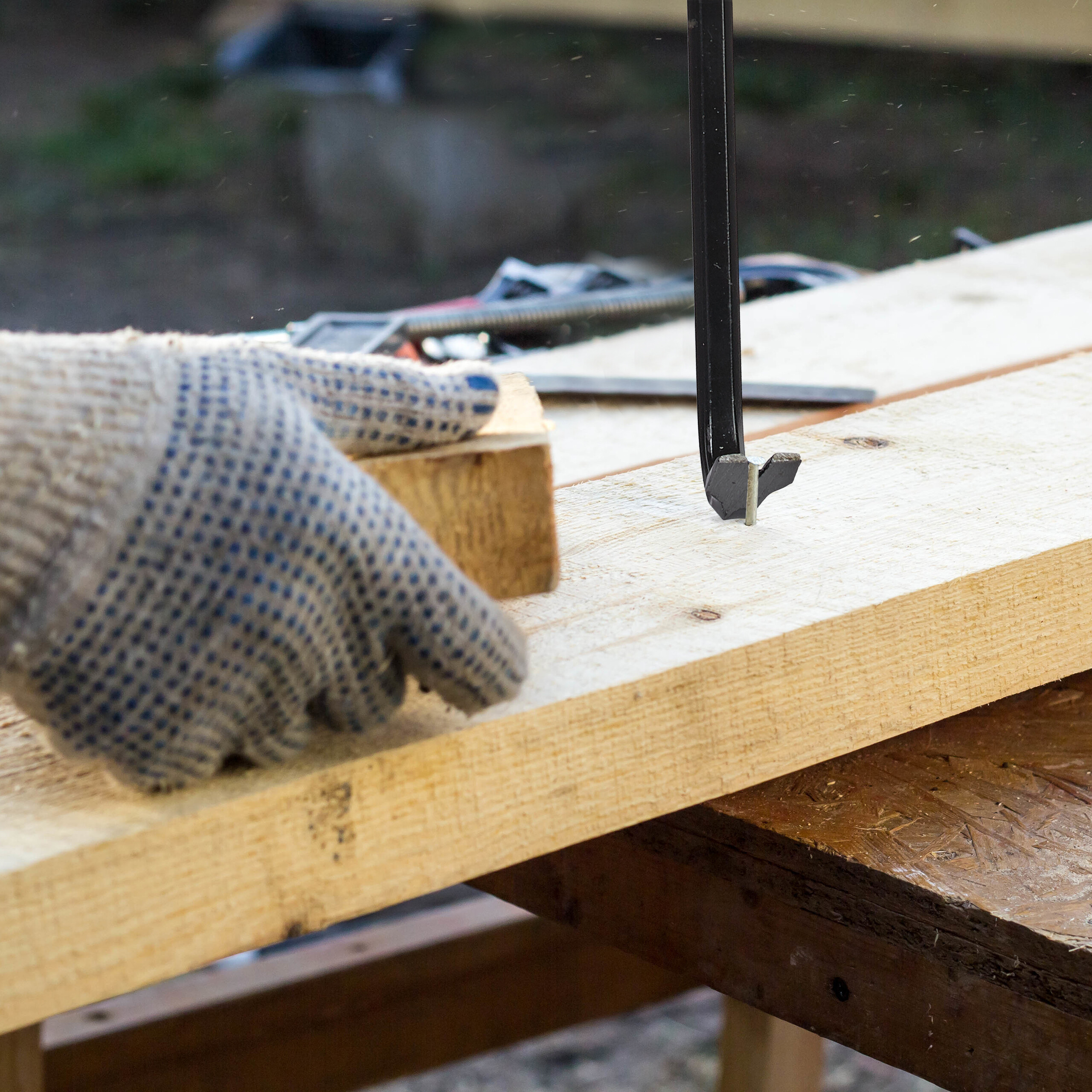 Eine behandschuhte Hand legt einen Holzblock auf ein Brett, während ein Meißel in eine Lasche schlägt.