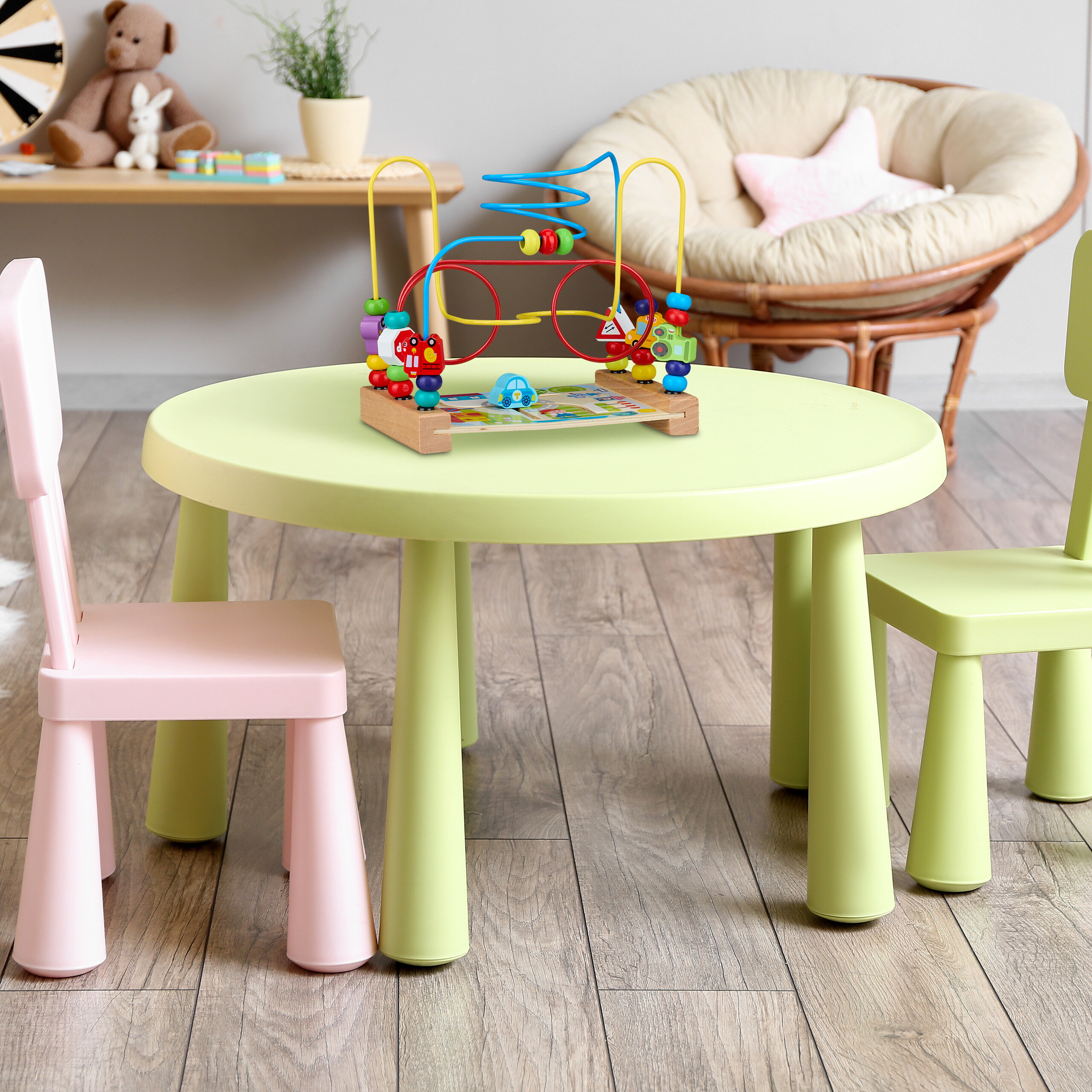 Ein hölzernes Motorikspielzeug steht auf einem runden grünen Kindertisch zwischen zwei kleinen Stühlen.