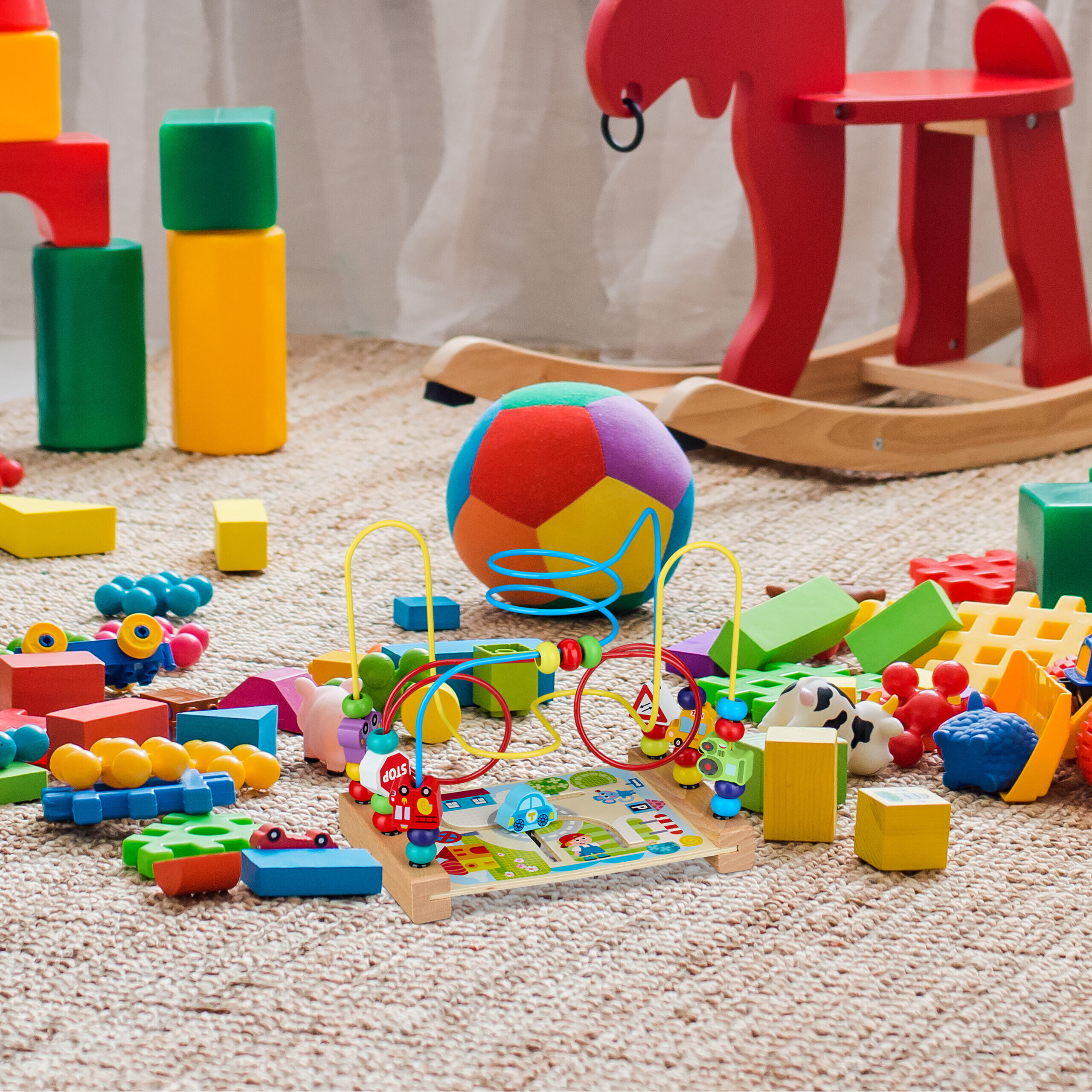 Bunte Holzspielzeuge und eine Ball auf einem Teppich im Kinderzimmer.