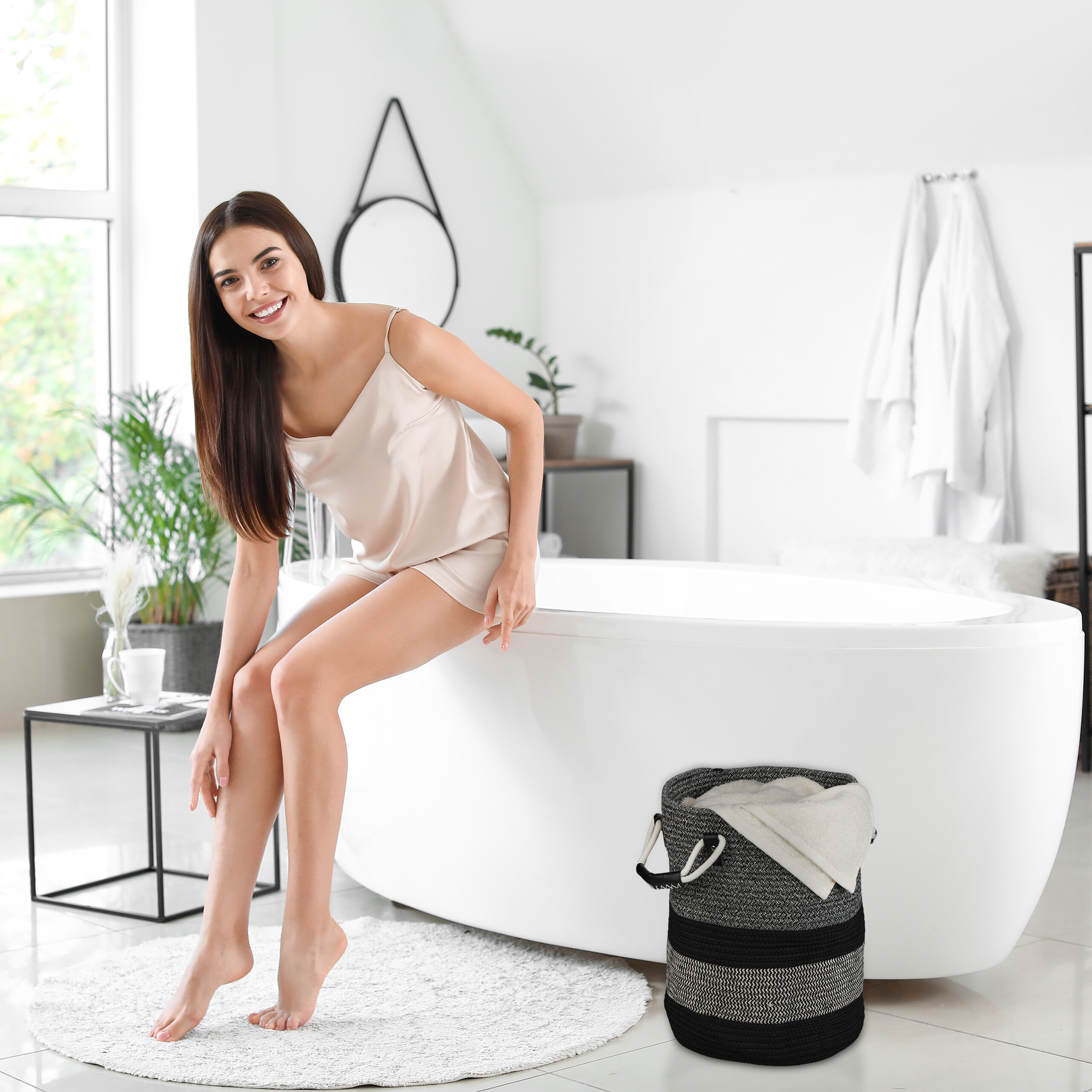 Eine lächelnde Frau in Seidenbekleidung sitzt am Rand einer weißen Badewanne in einem hellen, modernen Badezimmer.