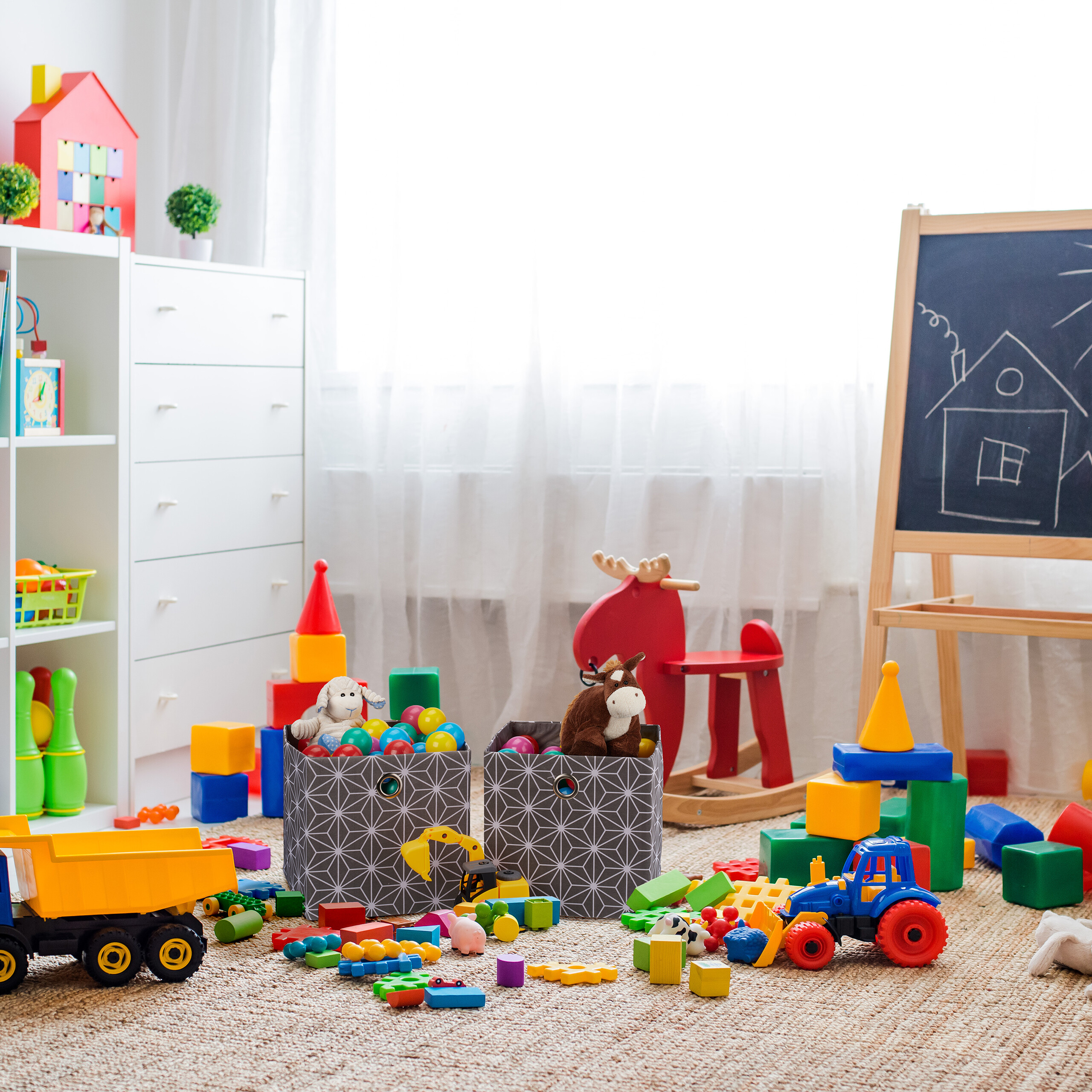 Ein buntes Spielzimmer mit Spielzeug, Kisten, einem roten Schaukelrentier und einer Tafel.