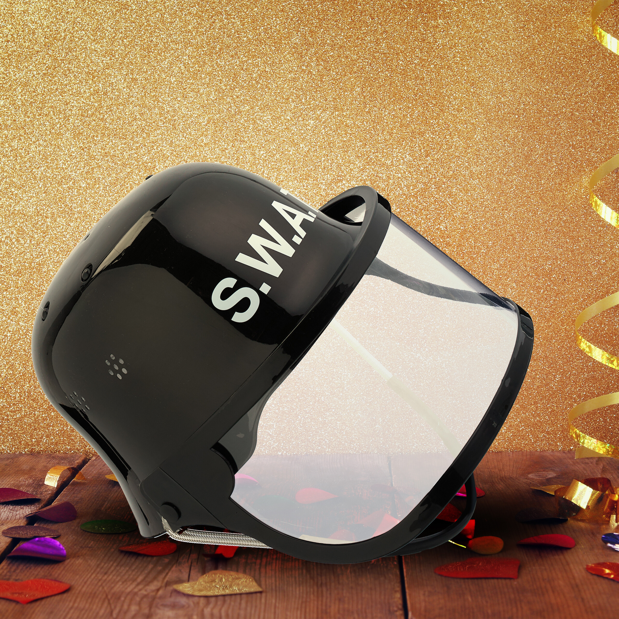 Ein schwarzer S.W.A.T.-Helm mit Visier liegt auf Holz, umgeben von Konfetti und vor glitzerndem Hintergrund.