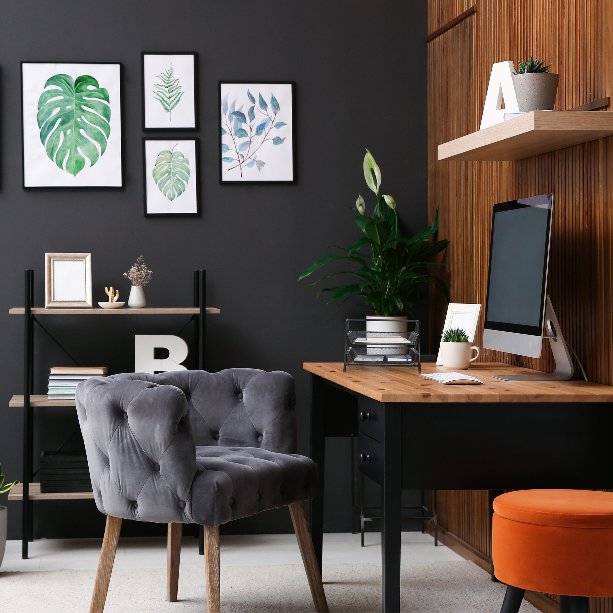 Moderne Büro-Innenausstattung mit Holztisch, grauem Sessel und Kunstpflanzen an dunkler Wand.