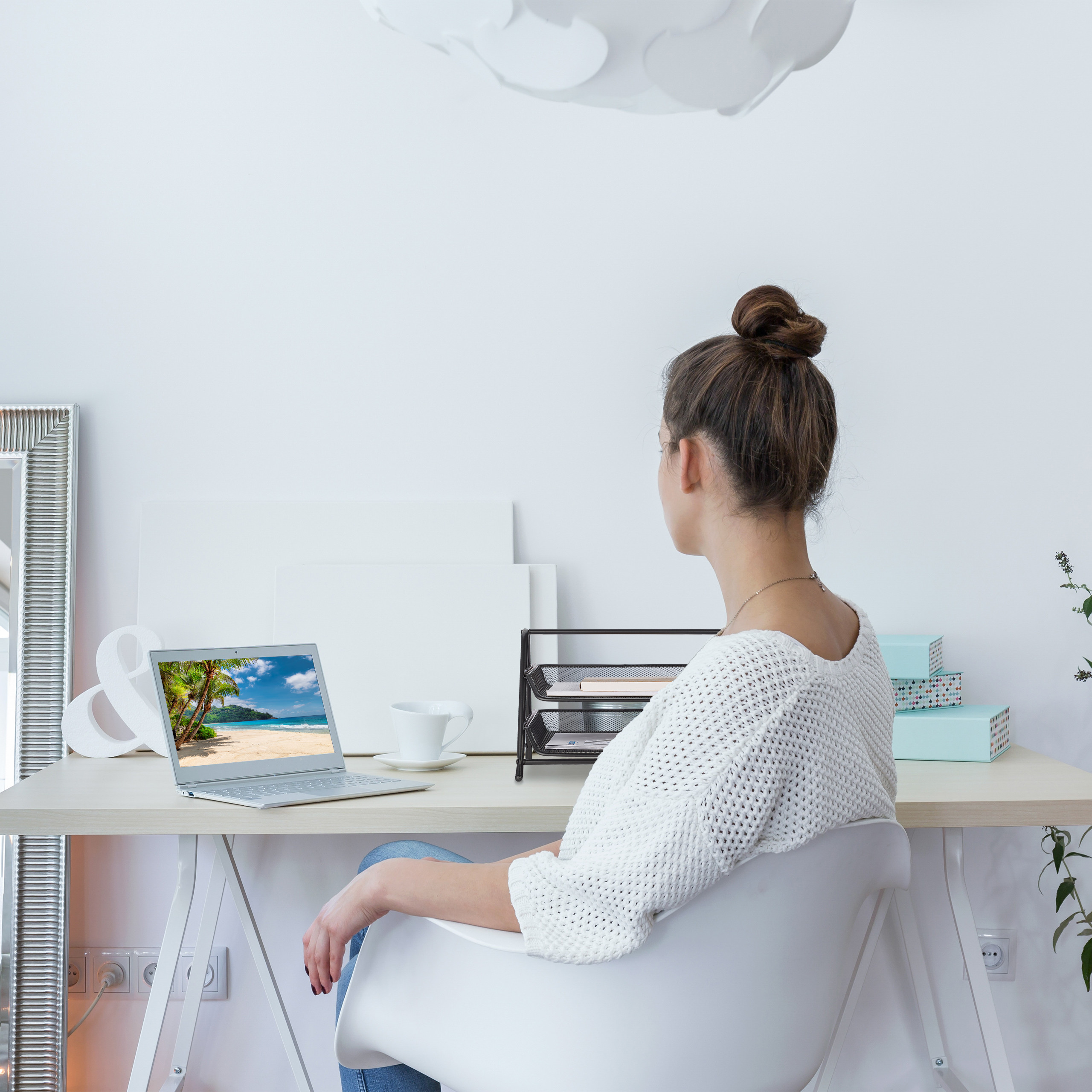 Eine Frau in einem weißen Pullover sitzt an einem Schreibtisch mit Laptop und blickt in den Raum.