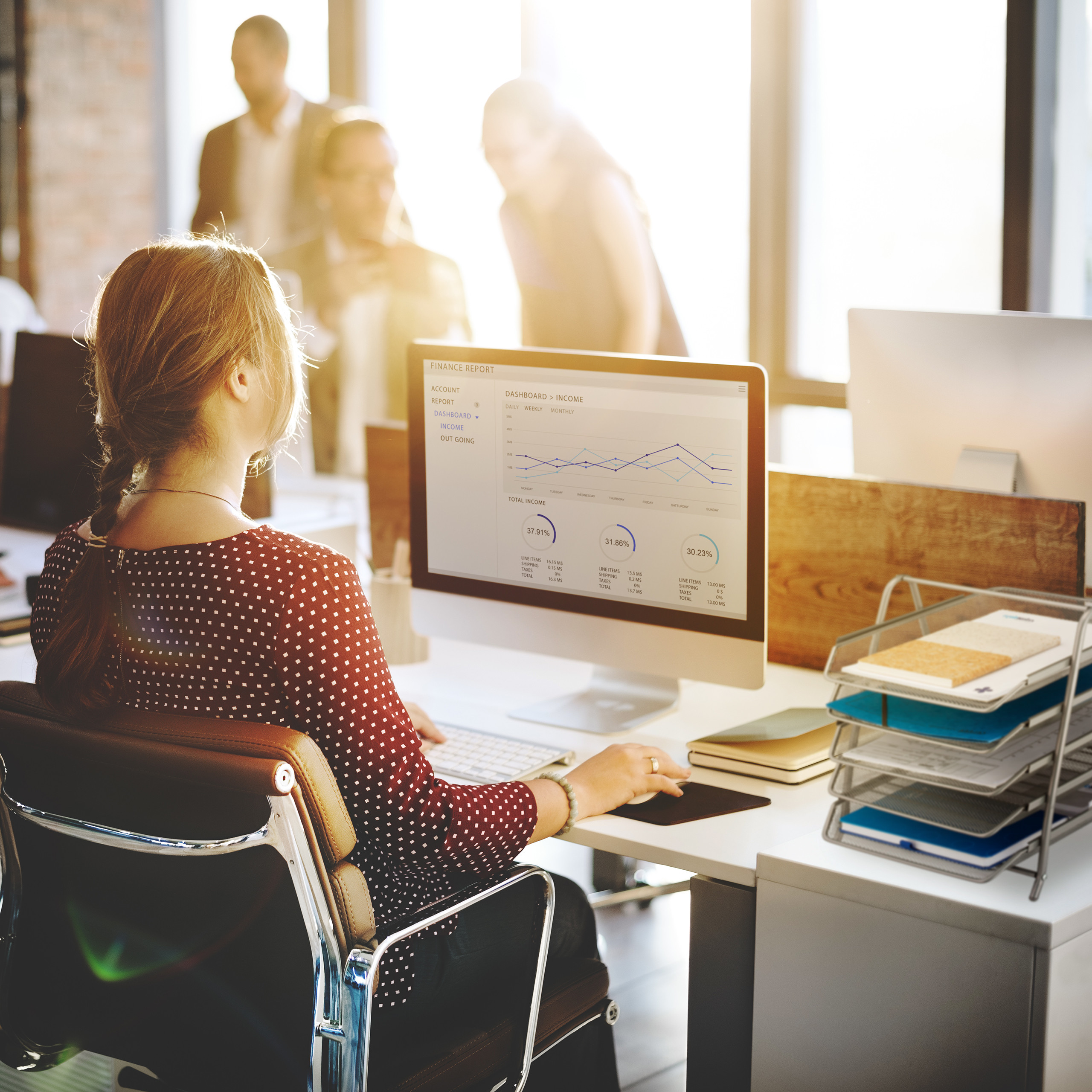 Frau mit rotem gepunktetem Oberteil arbeitet im sonnigen Büro an einem Computer.