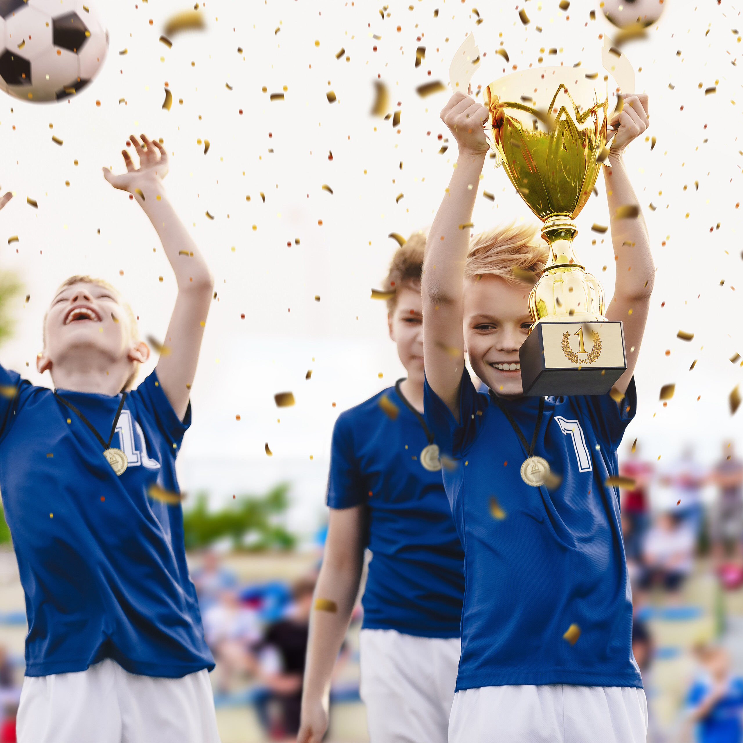 Junge in blauer Kleidung hält glänzenden Pokal, umgeben von fallendem Konfetti und lächelnden Mannschaftskameraden.