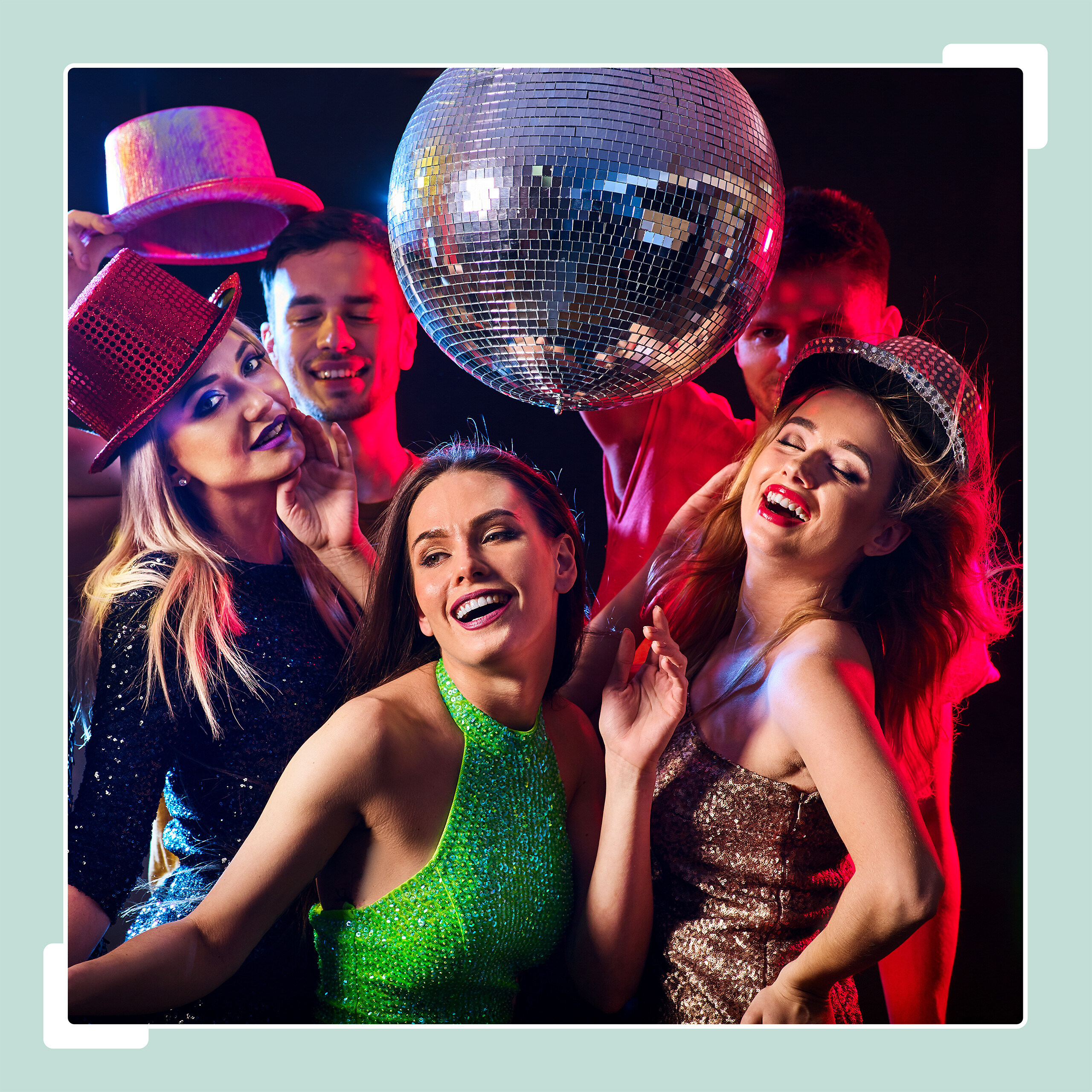 Glückliche Freunde in Partykleidung posieren unter einer glänzenden Discokugel in bunter Beleuchtung.