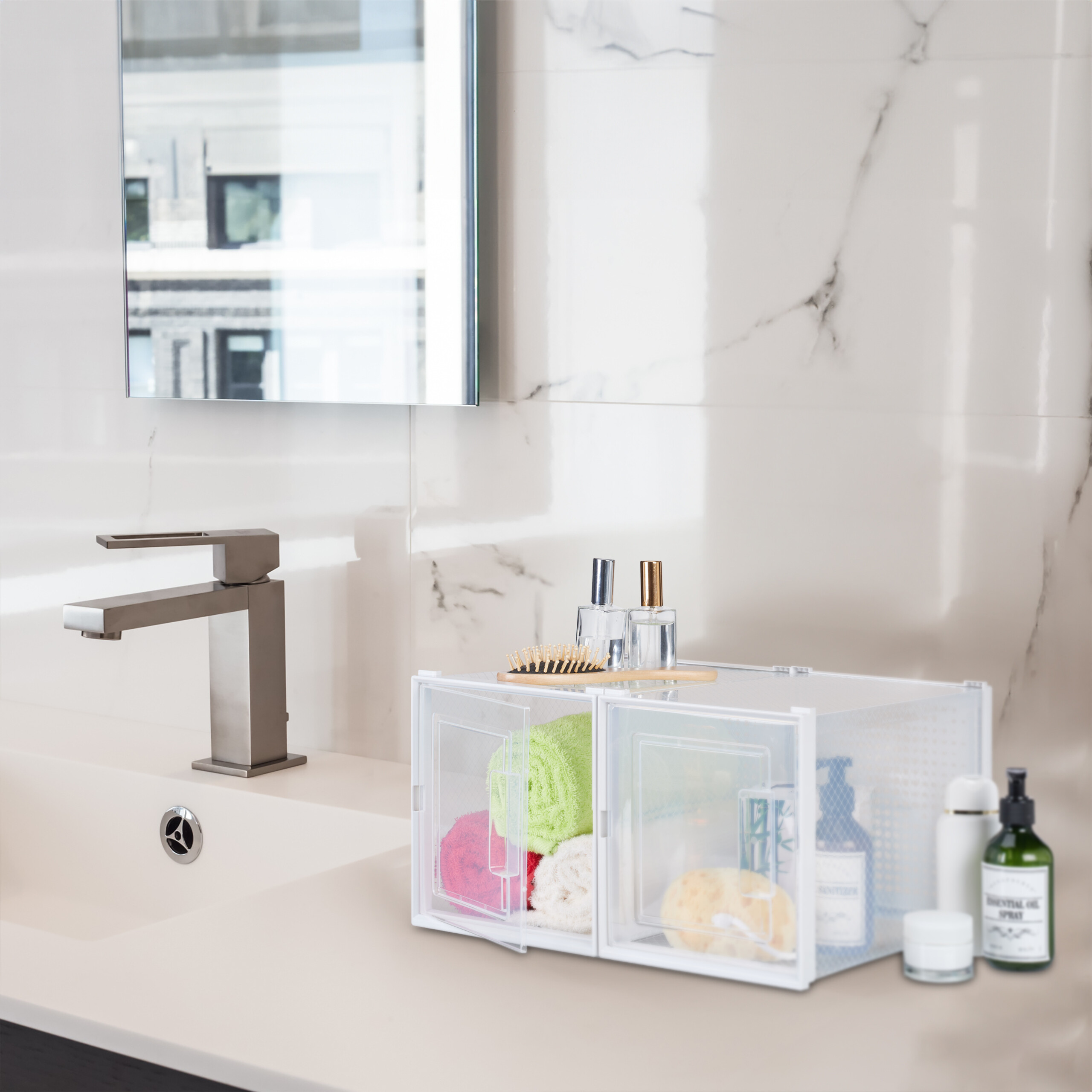 Ein weißer Marmor-Badezimmertisch mit Waschbecken, Armatur, Spiegel und zwei klaren Plastikboxen mit Handtüchern.