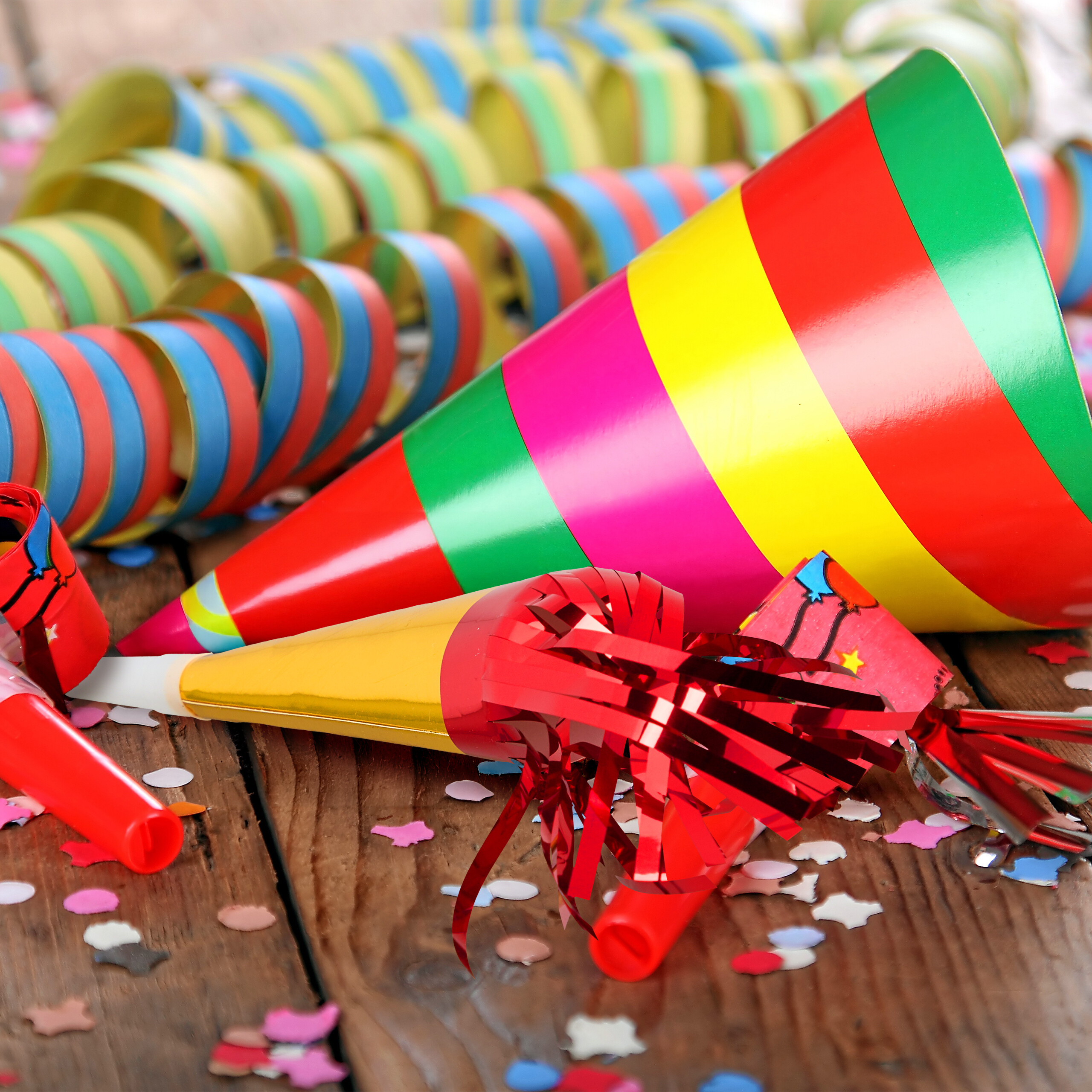 Bunte Partyhüte, Luftschlangen und Konfetti auf einer Holzoberfläche.