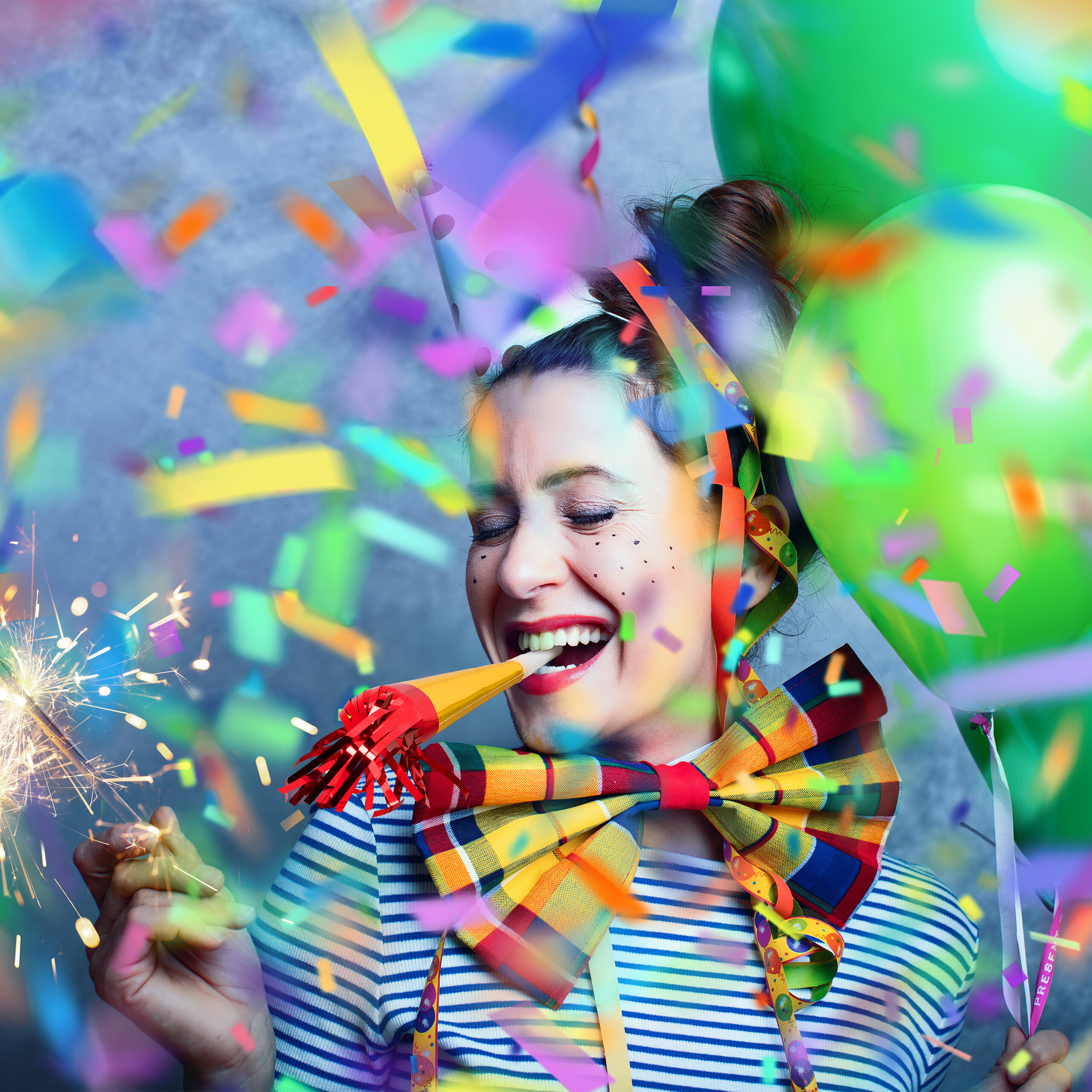Eine Frau feiert mit Partytüte, Wunderkerze, Luftballons und bunten Konfetti.