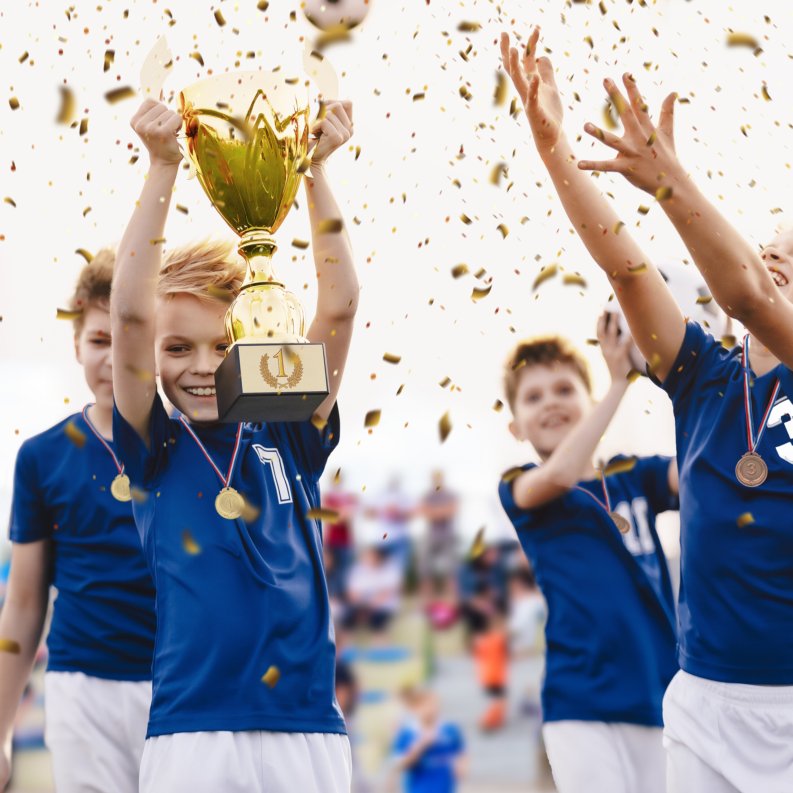 Junge hält einen goldenen Pokal hoch, während Konfetti und andere Spieler im Hintergrund feiern.