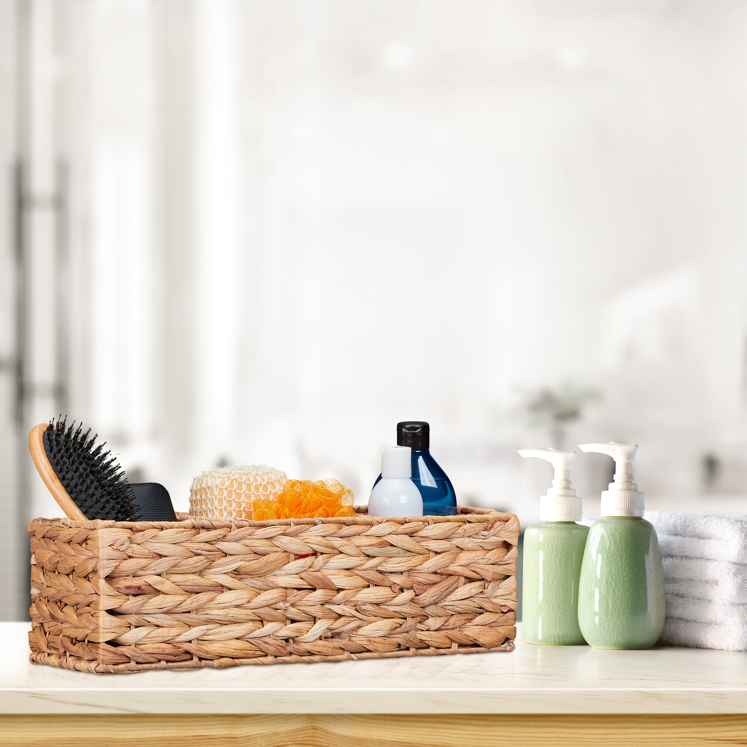 Weidenkorb mit Haarbürste, Schwämmen und Flaschen auf weißer Theke neben grünen Seifenspendern und gefalteten weißen Handtüchern.