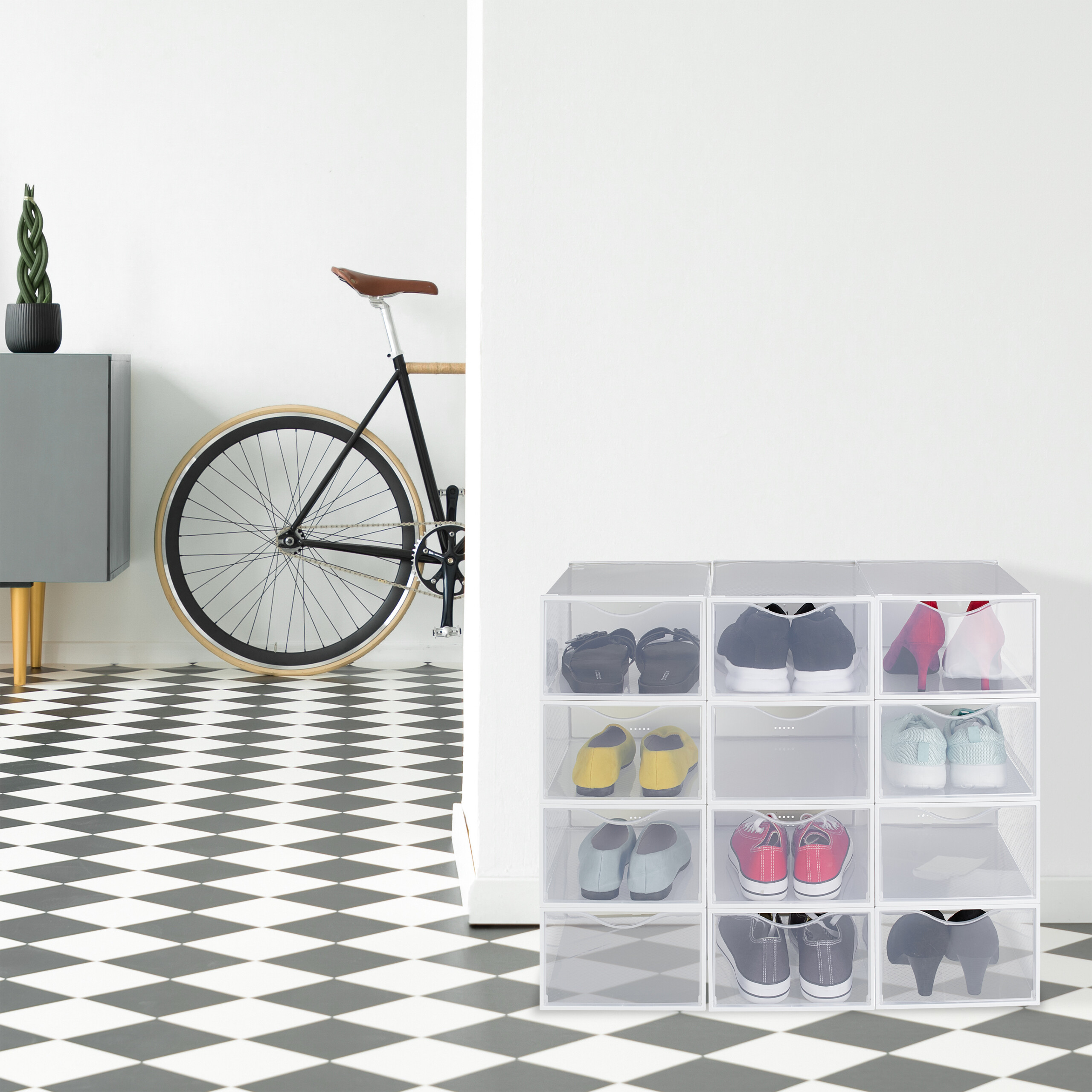 Modulare transparente Schuhregale auf schwarz-weißem Schachbrettboden, im Hintergrund ein Fahrrad.
