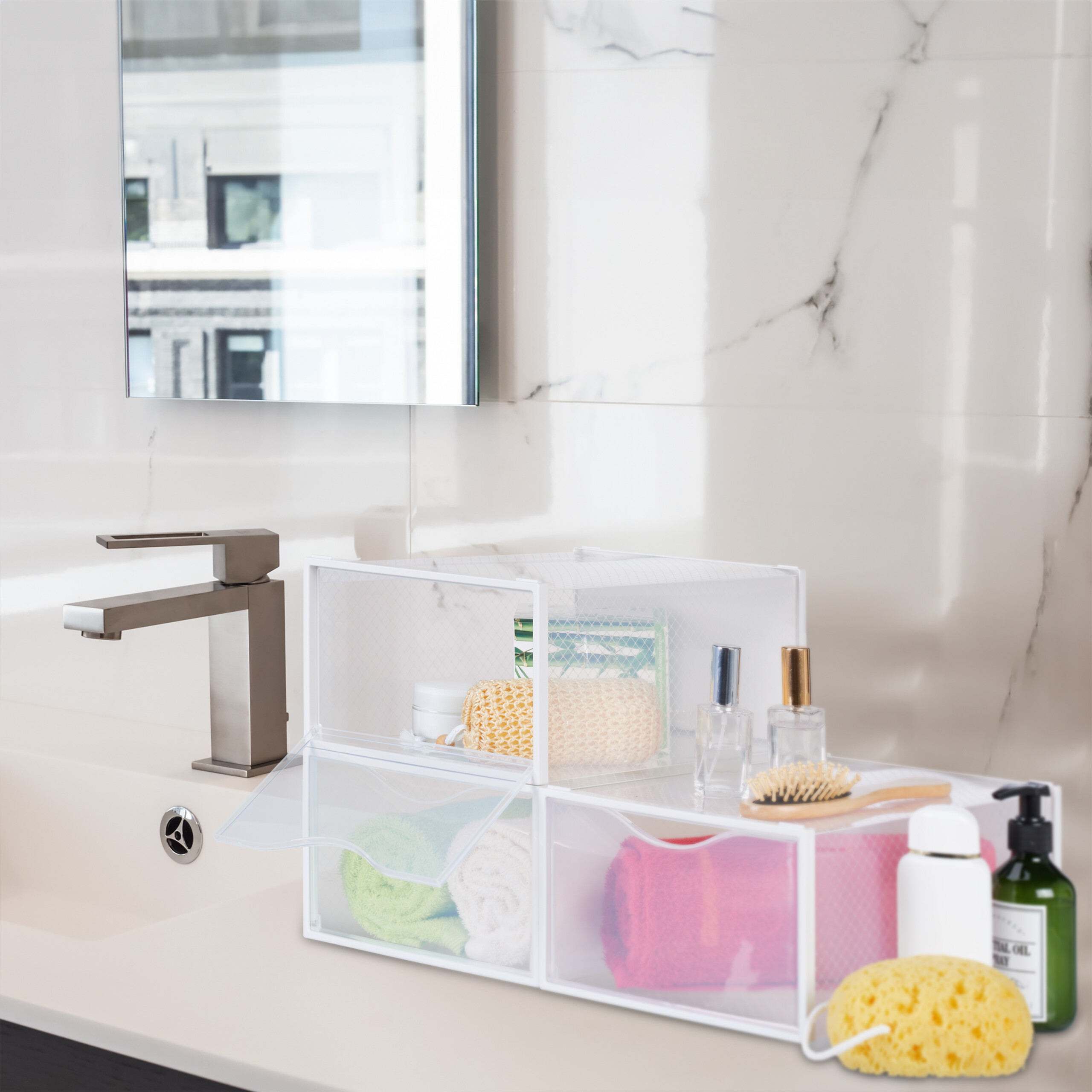 Transparente Organizerboxen auf einer Badezimmertheke mit Handtüchern, Toilettenartikeln und einem Waschbecken.