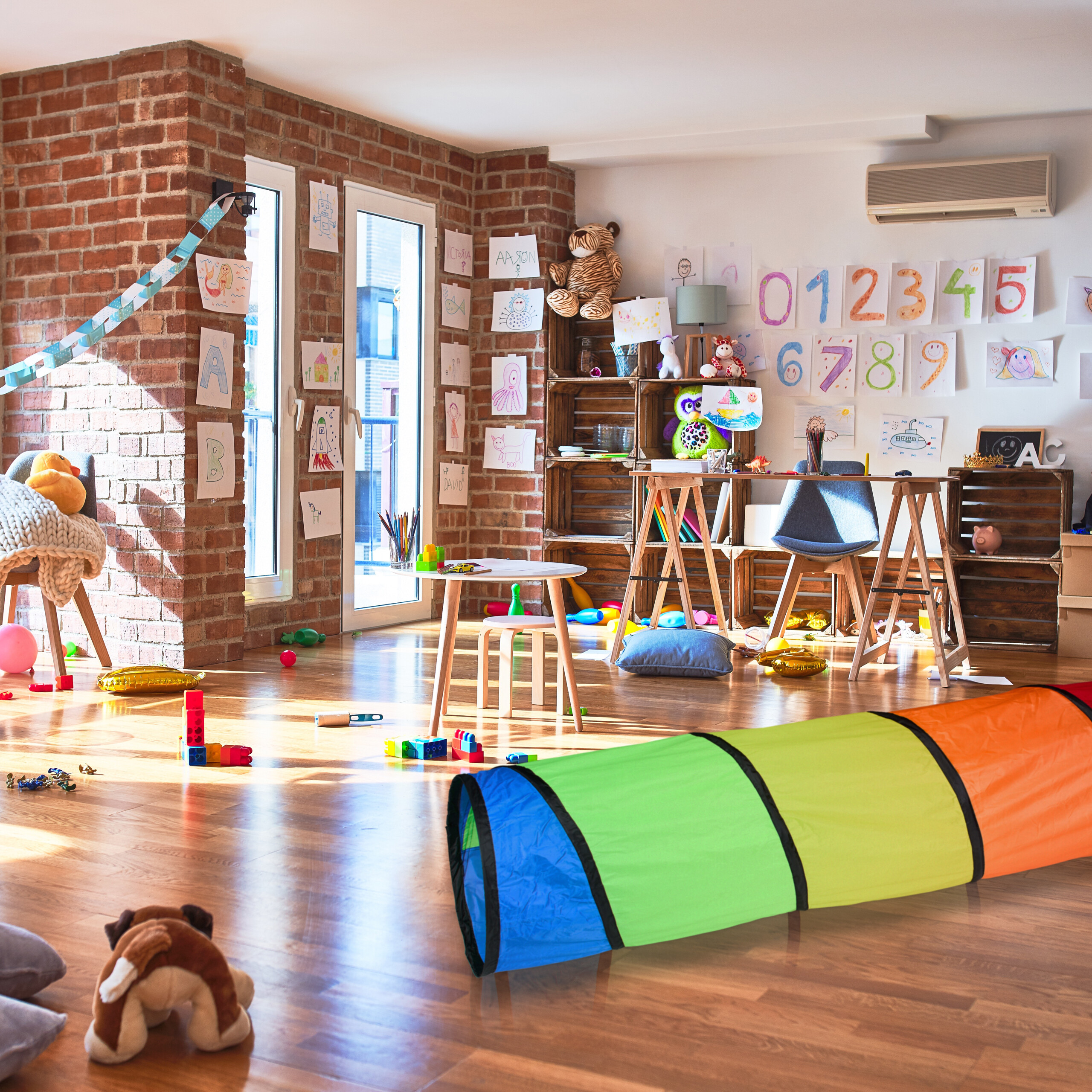 Buntes Kinderspielzimmer mit Holzboden, Spielzeug, Zeichnungen an der Wand und einem großen Kriechtunnel.