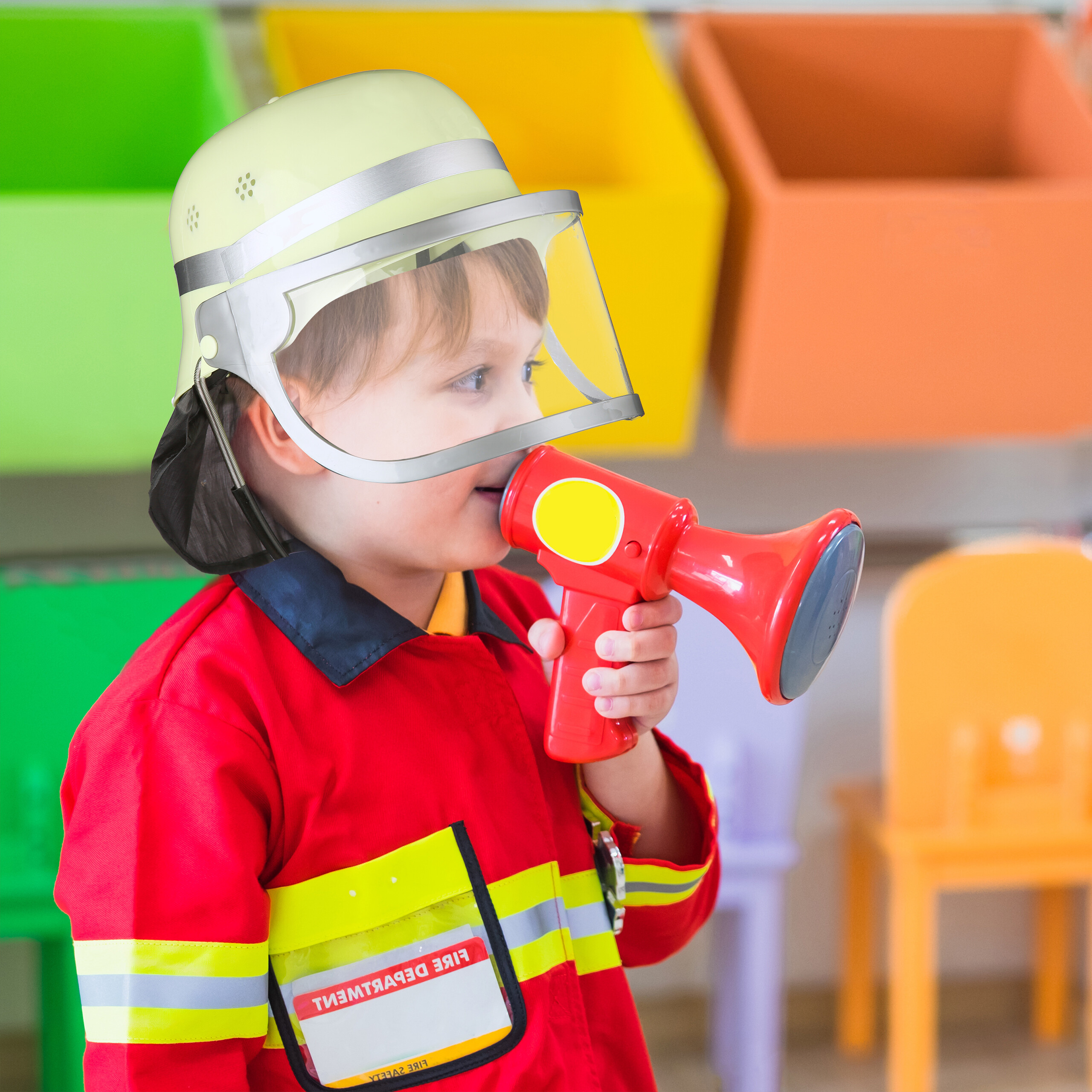 Kind in Feuerwehruniform mit Helm hält einen roten Megafon in einem bunten Raum.