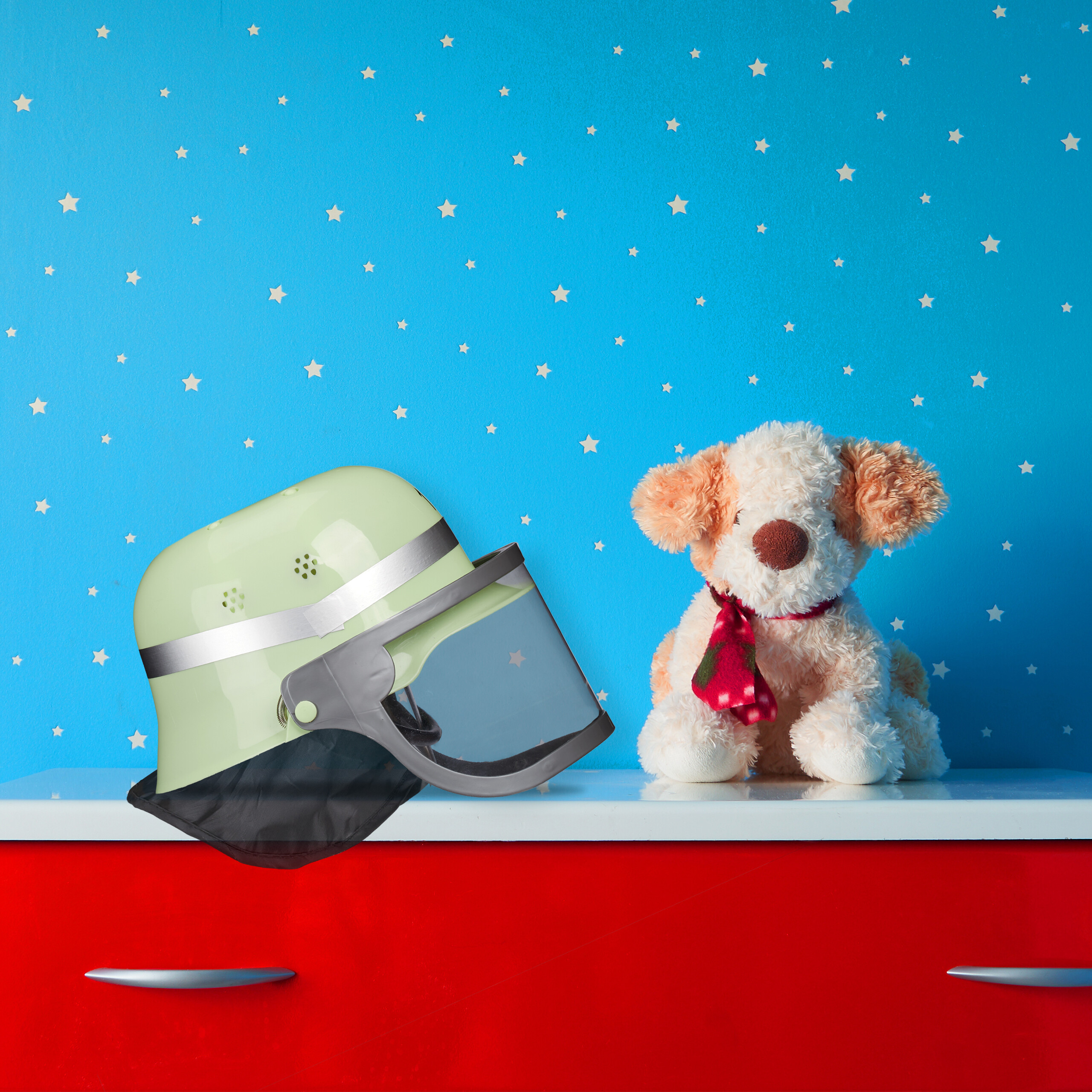Ein Feuerwehrhelm und ein Plüschhund auf einer roten und weißen Kommode vor einer blau-weißen Sternenwand.