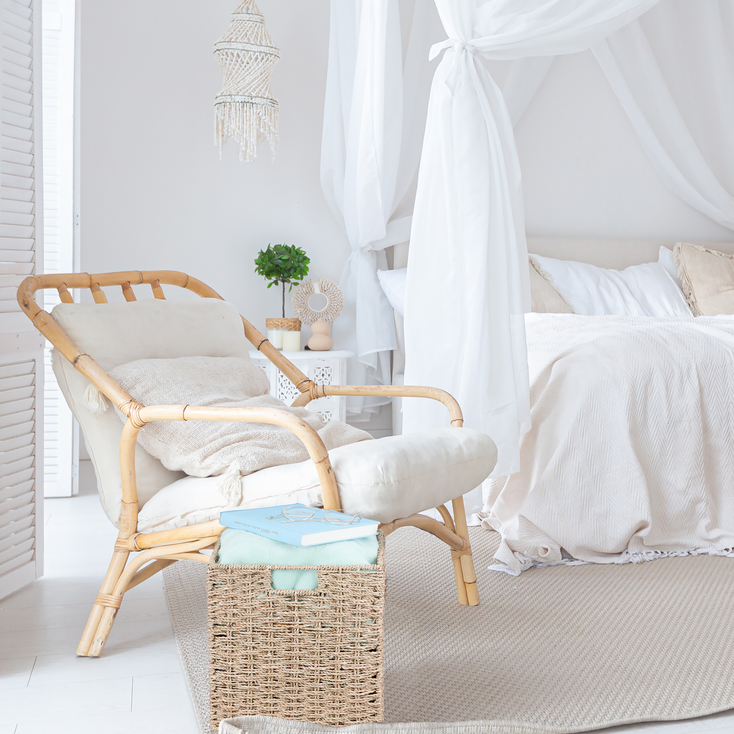Ein gemütliches Schlafzimmer mit Rattan-Sessel, hellem Bett mit Baldachin, Korb und makramee-Lampe in Weiß.