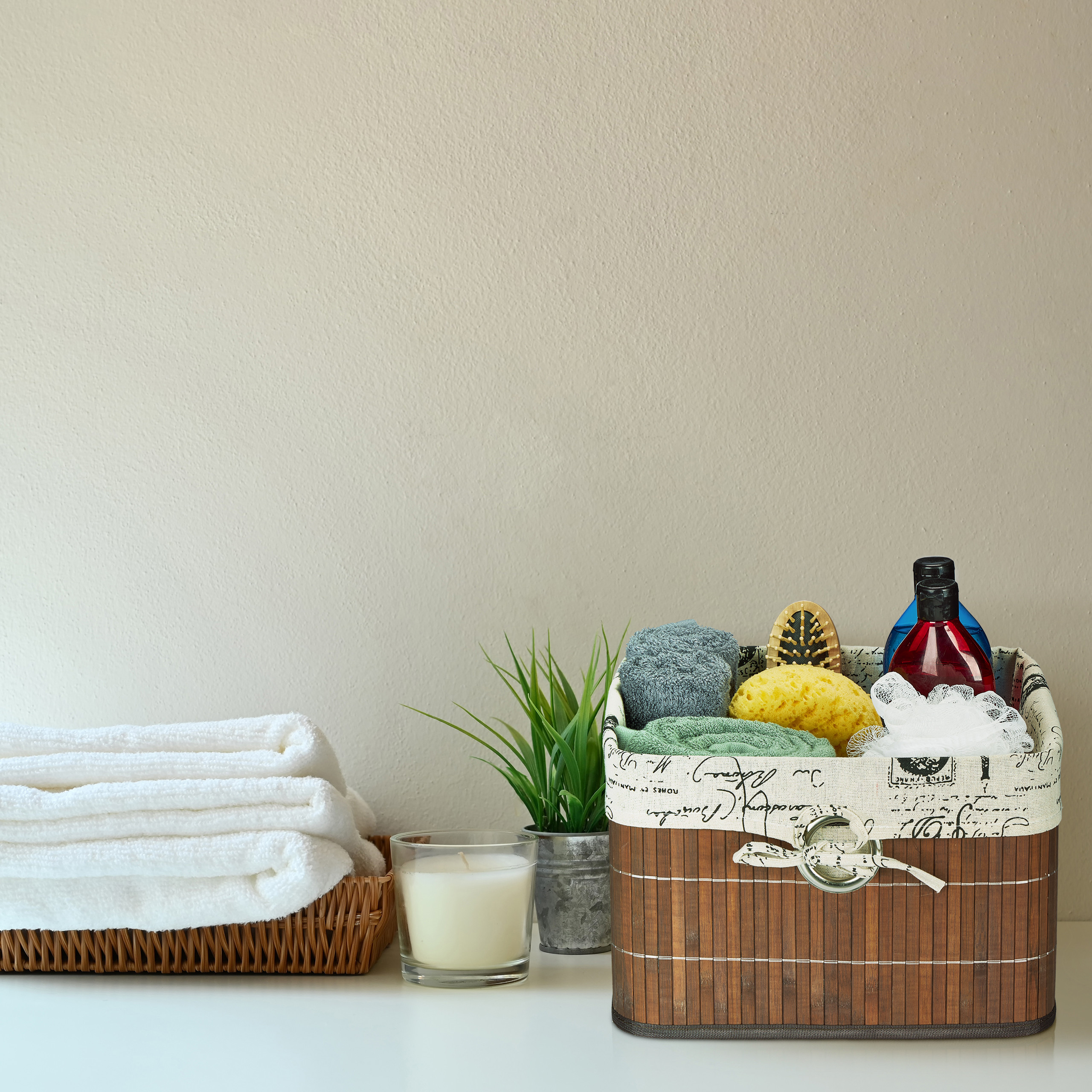 Ein Holzkorb mit Badutensilien, eine Kerze, ein Blumentopf und gefaltete weiße Handtücher in einem Korb auf einem Tisch.