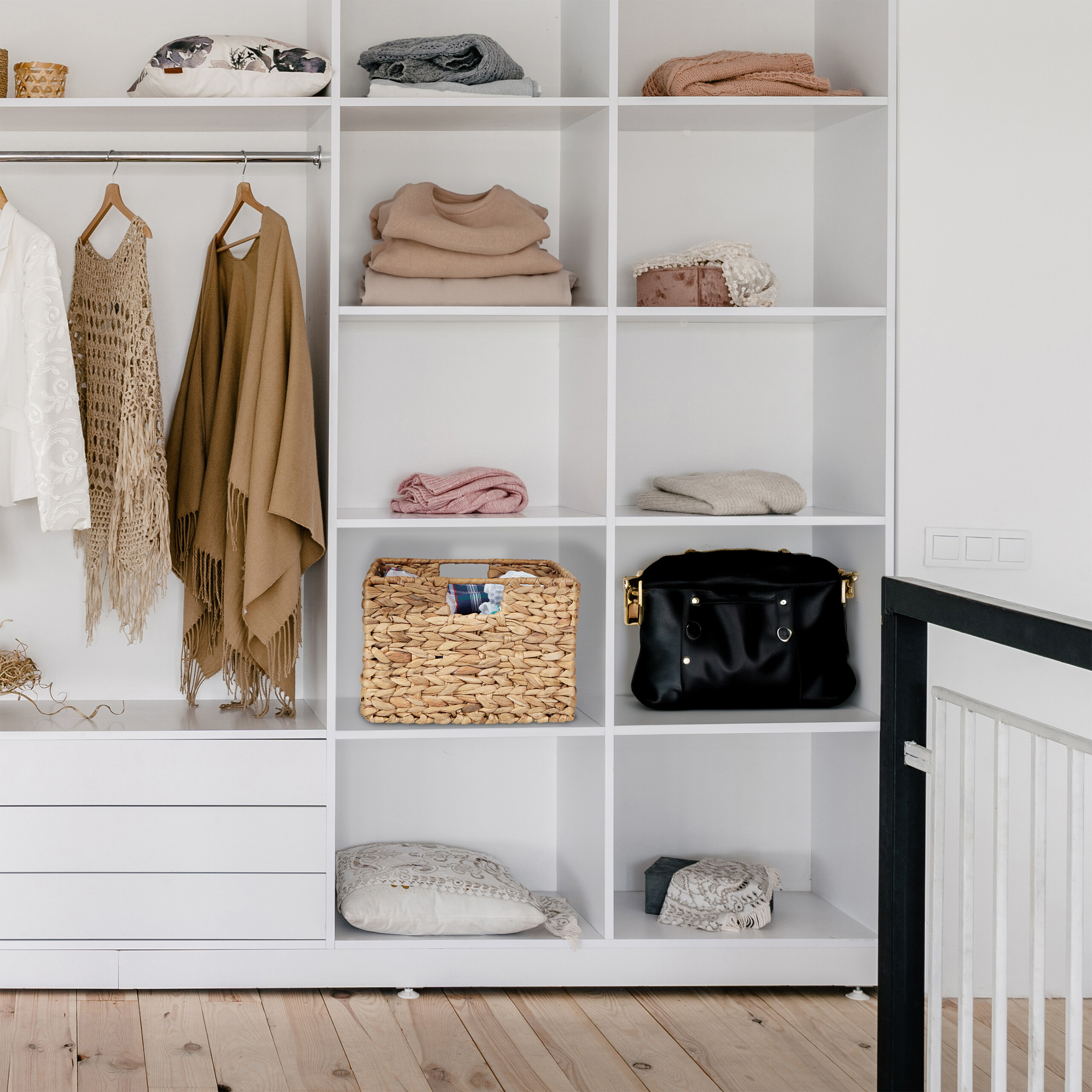 Ein weißer Kleiderschrank mit gefalteter Kleidung, Hängewaren, einem Weidenkorb und einer schwarzen Tasche.
