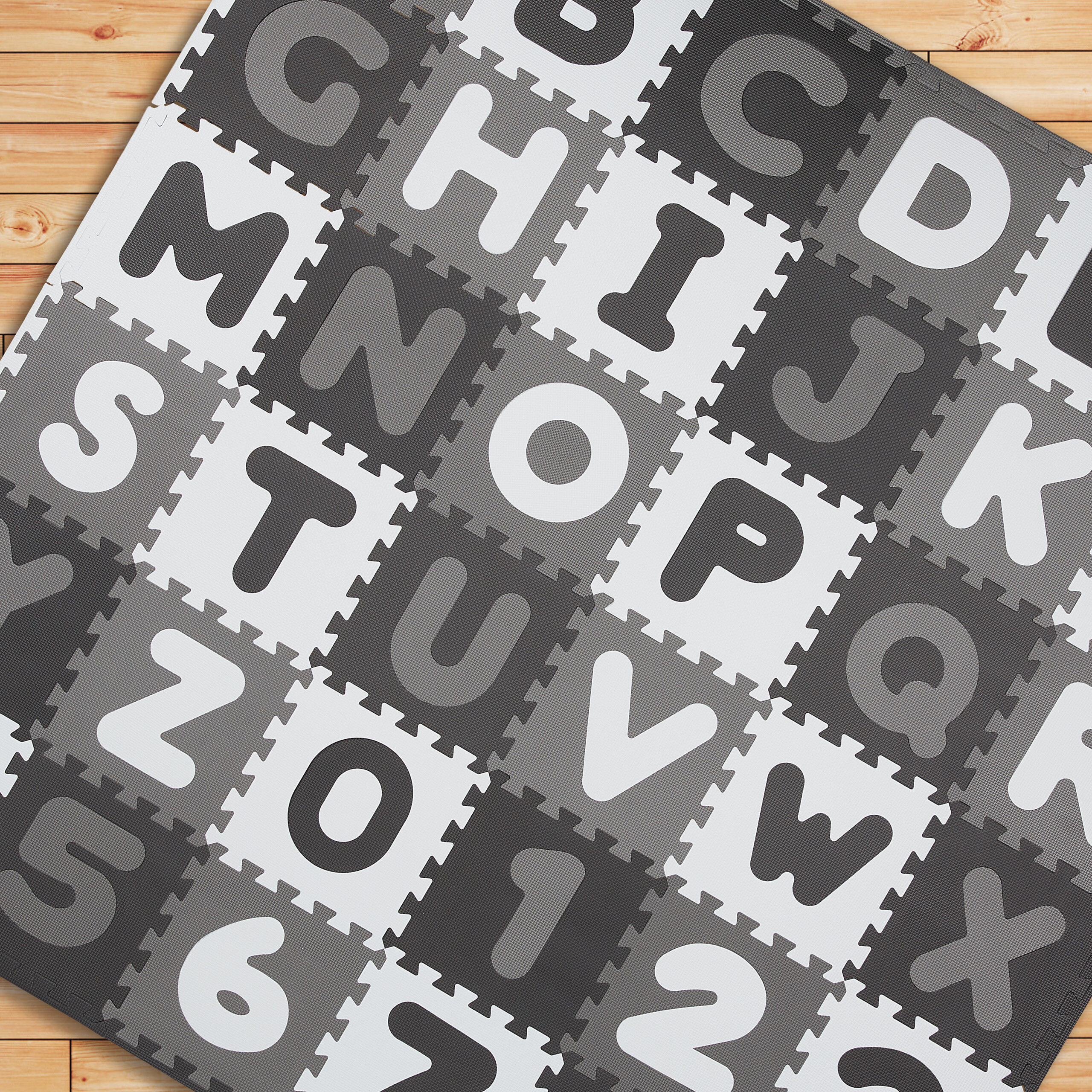 Graue und weiße Schaumstoff-Spielmatten mit Alphabet- und Zahlenbuchstaben auf einem Holzfußboden.
