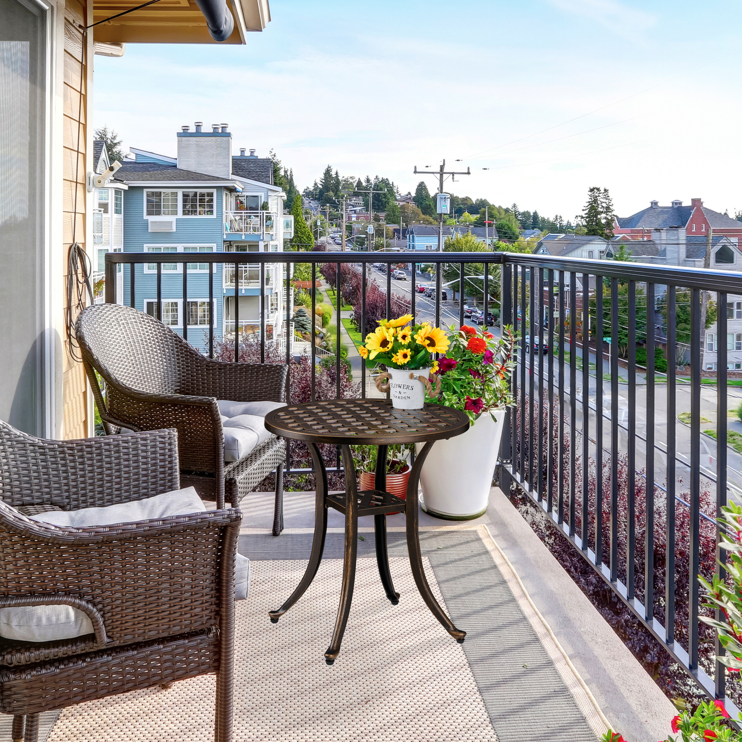 Ein sonniger Balkon mit zwei Korbstühlen, einem kleinen Tisch mit Blumen und Straßensicht im Hintergrund.