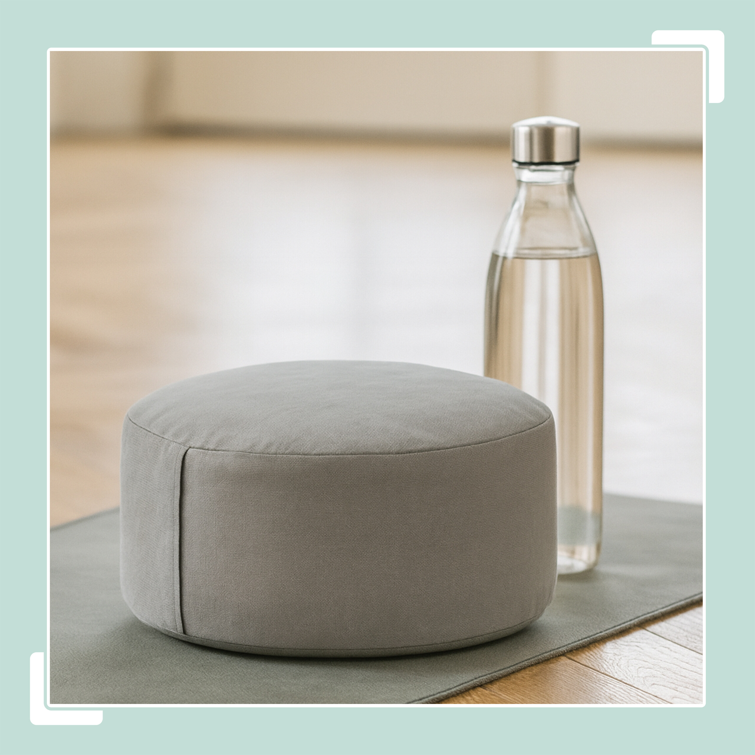 Ein graues Yogakissen und eine Glasflasche mit Wasser stehen auf einer Yogamatte auf Holzboden.