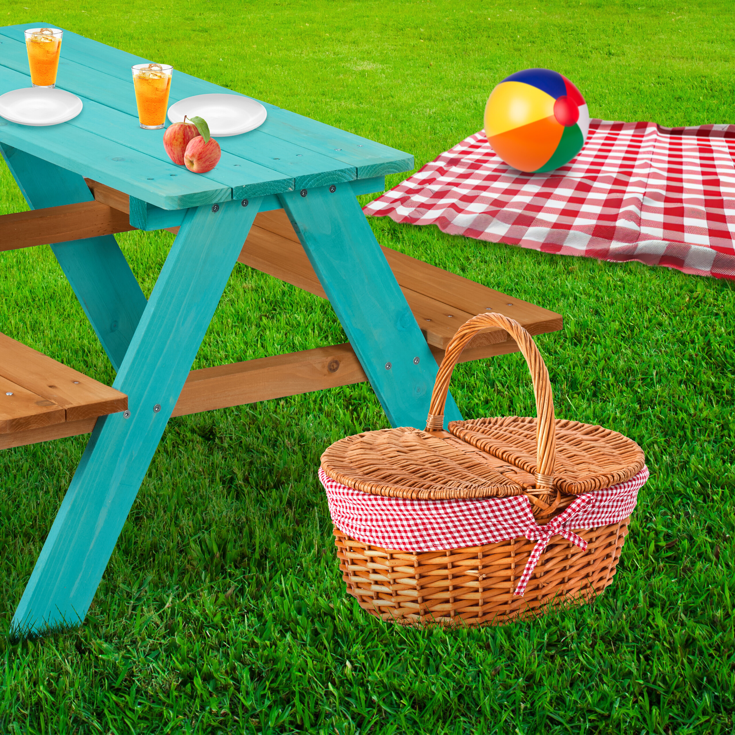 Picknicktisch mit Getränken, Äpfeln, Korb und roter Decke auf grünem Gras.