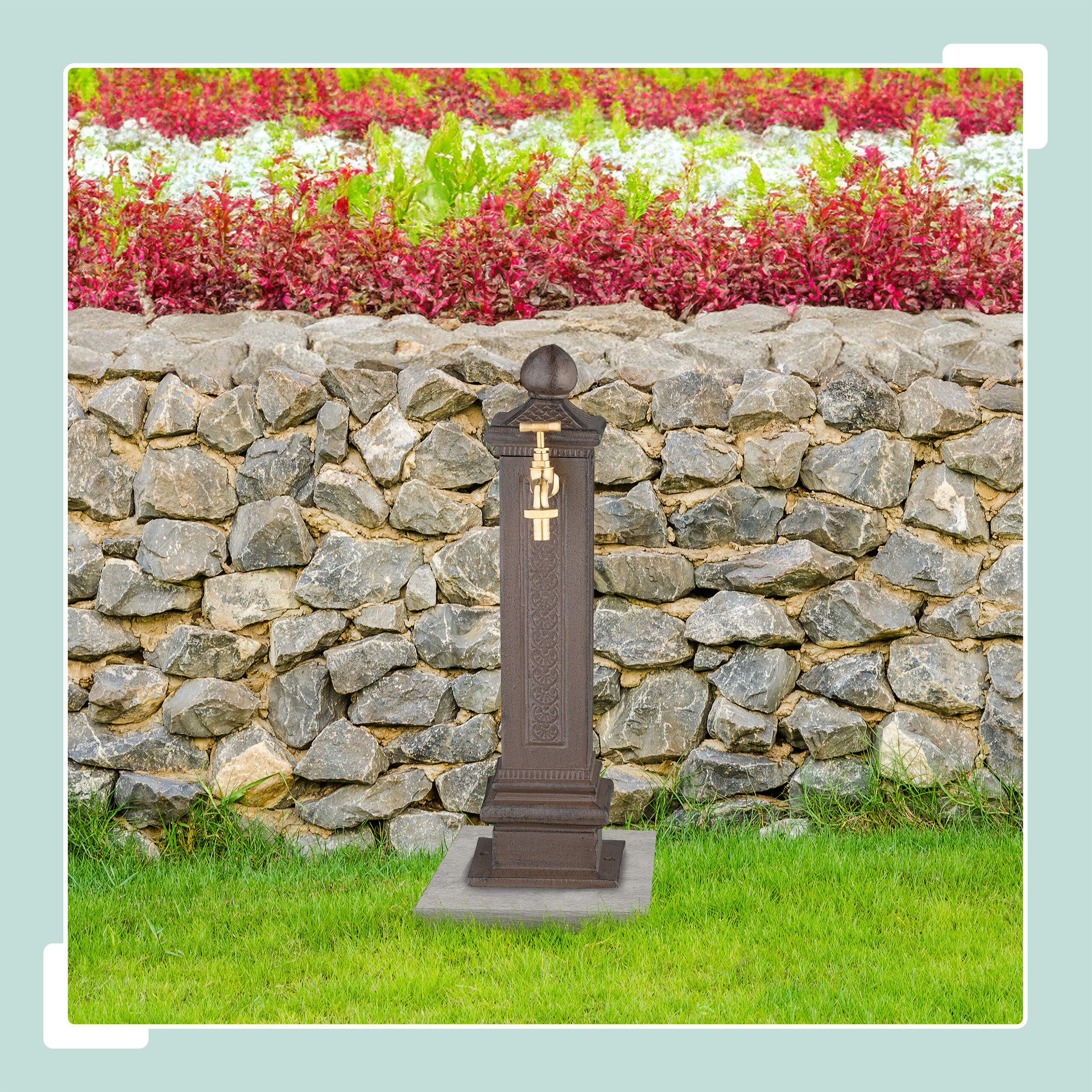 Ein dunkelbrauner Standbrunnen mit goldenem Wasserhahn vor einer Steinwand und Blumenbeet.