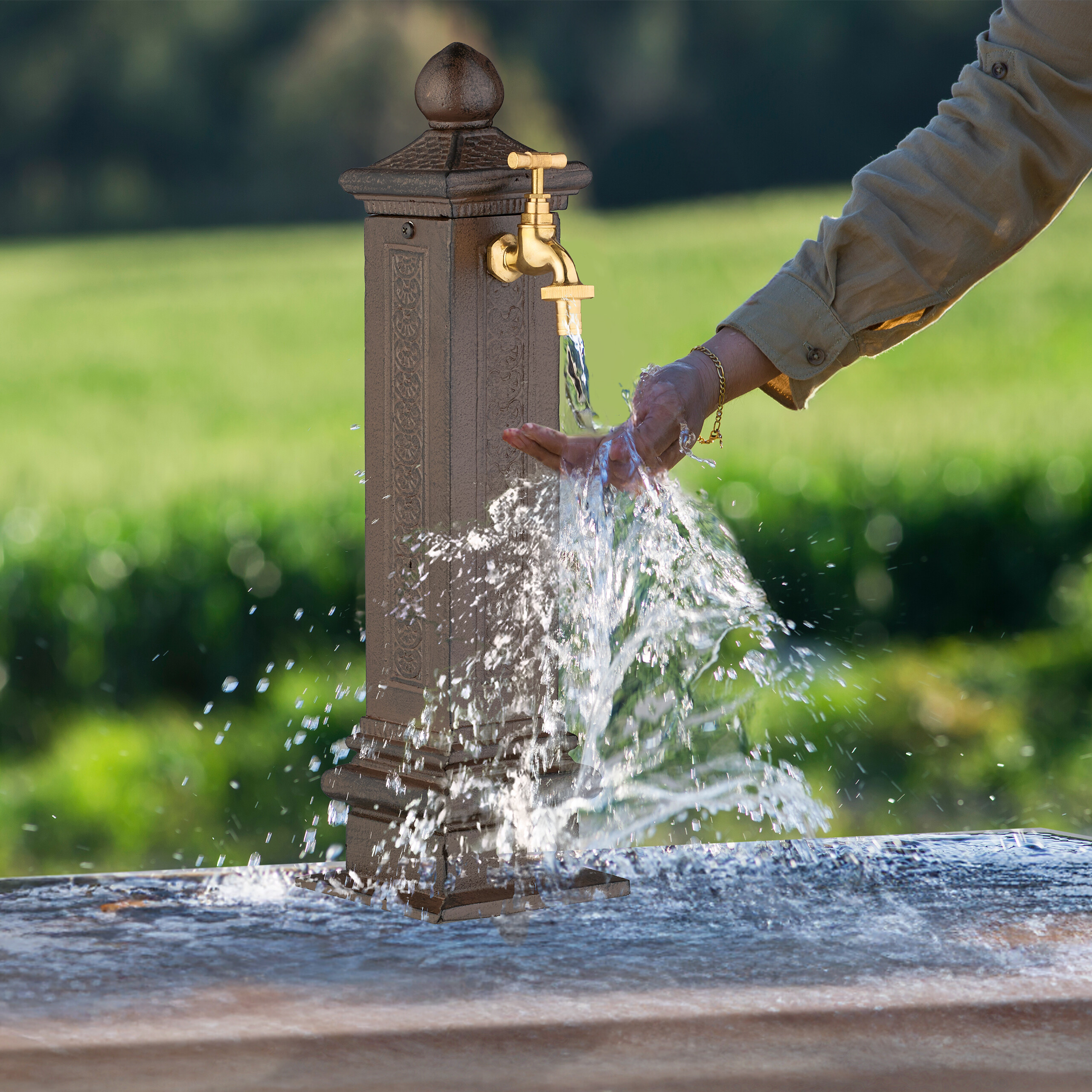 Eine Person wäscht sich die Hände in spritzendem Wasser aus einem Gartenbrunnen.