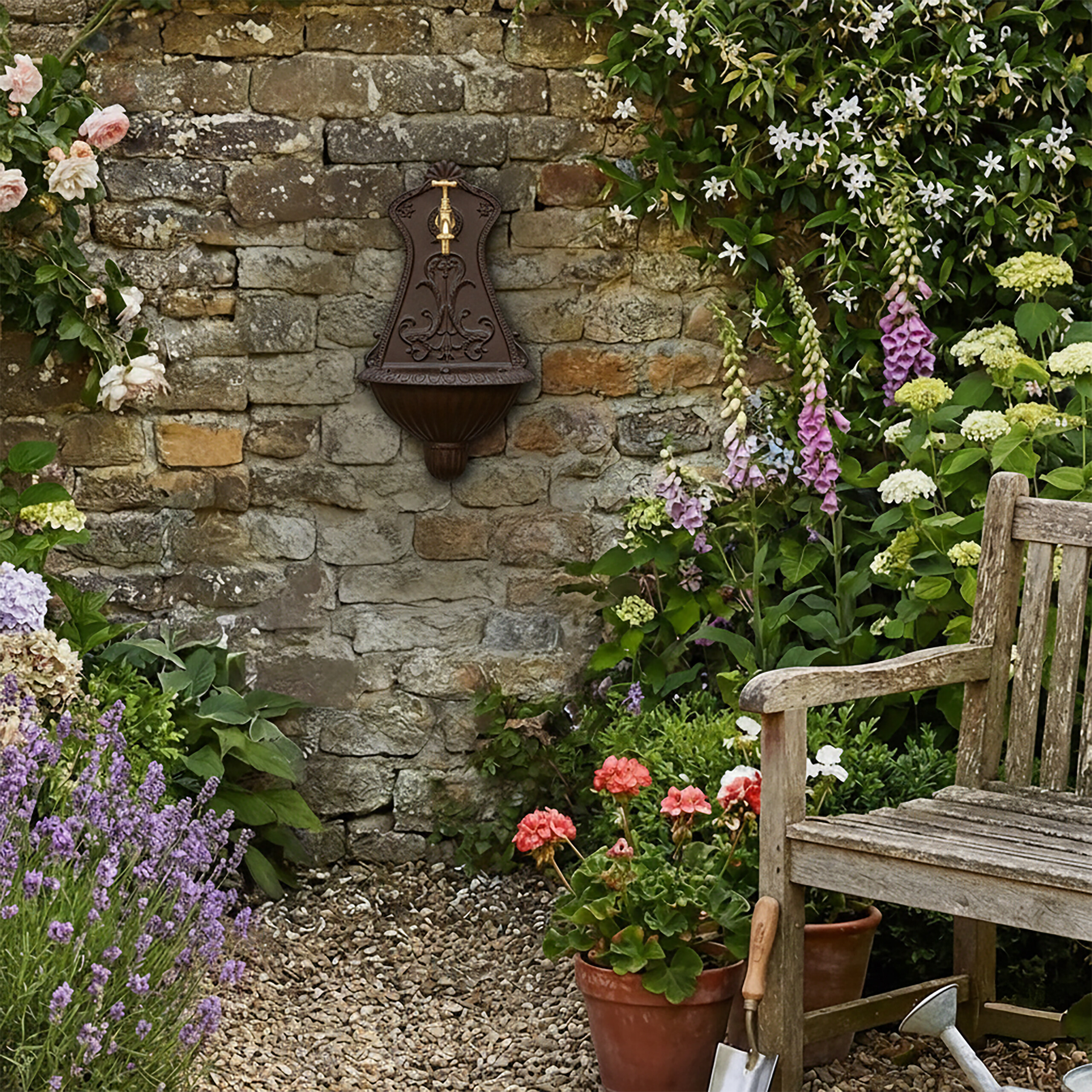 Ein antiker Wandbrunnen an einer Steinmauer, umgeben von bunten Blumen und einer Holzbank im Garten.