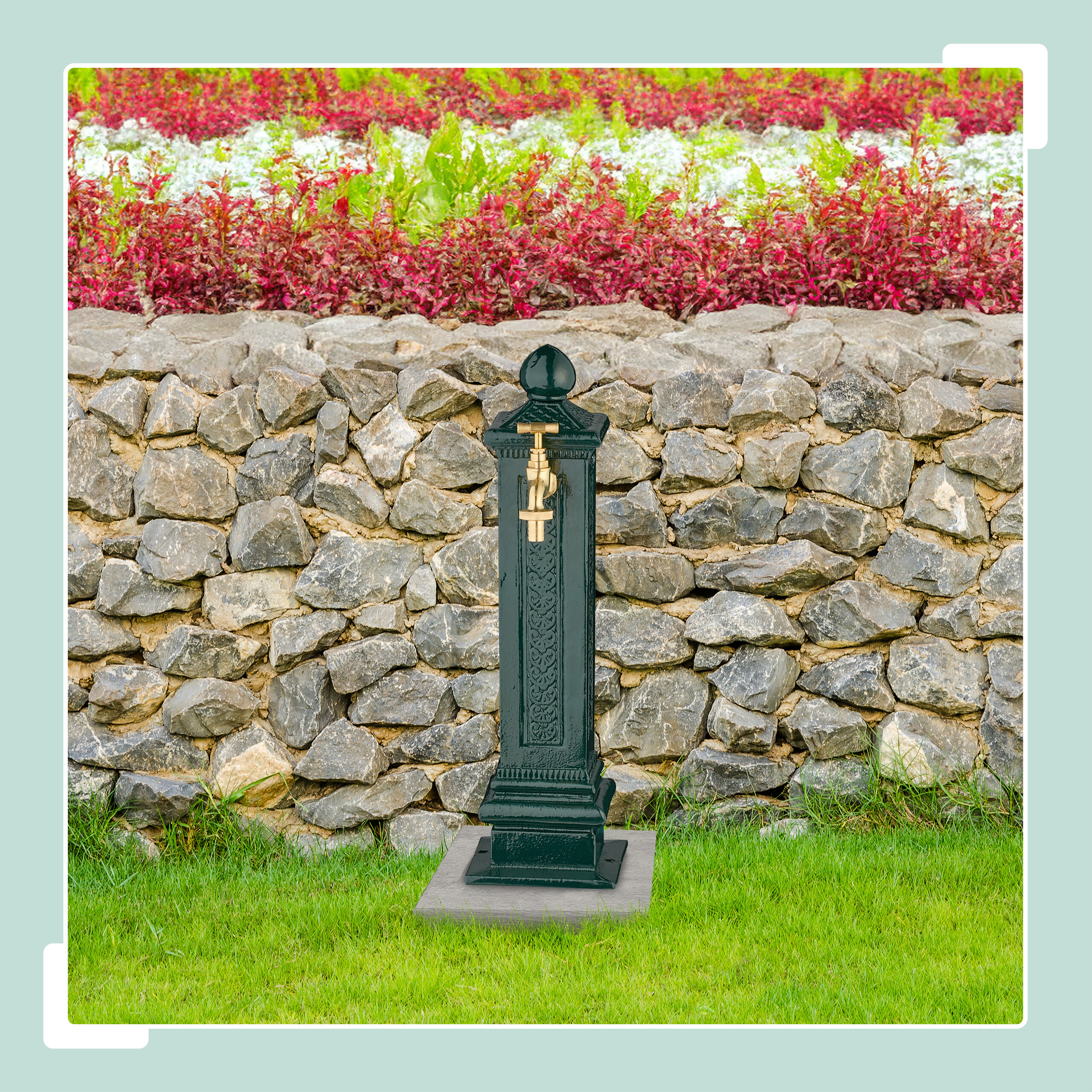 Ein dunkelgrüner Gartenbrunnen mit goldenem Wasserhahn vor einer Steinmauer.