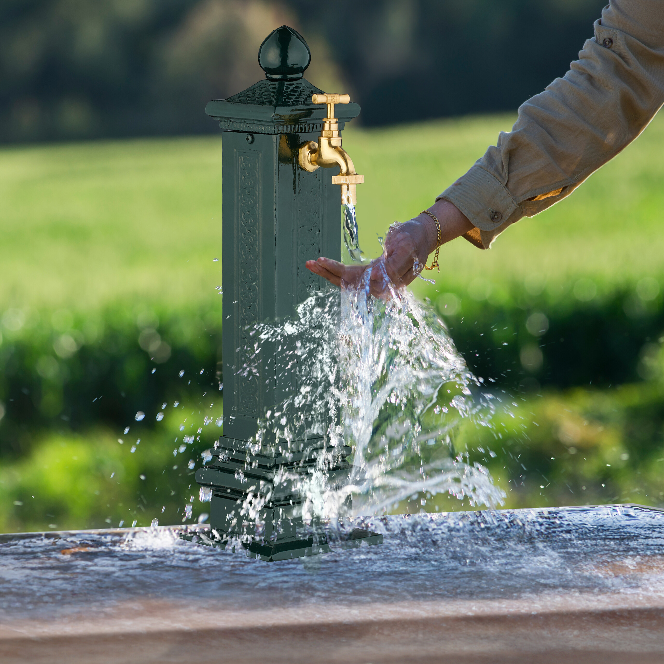 Eine Hand wäscht sich unter dem fließenden Wasser eines antiken grünen Gartenbrunnens.