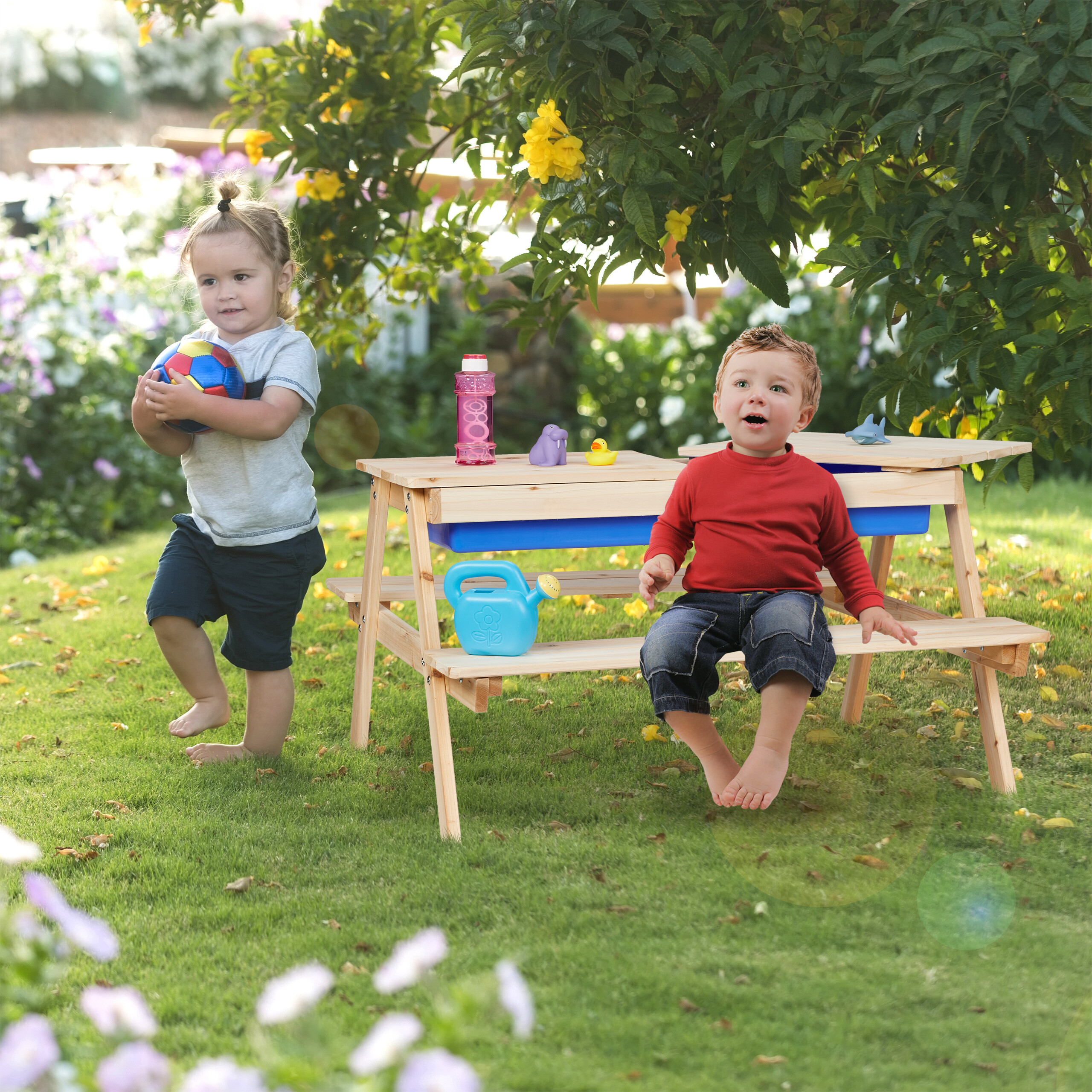 Zwei kleine Jungen spielen im Garten in der Nähe eines Holztisches unter einem belaubten Baum.