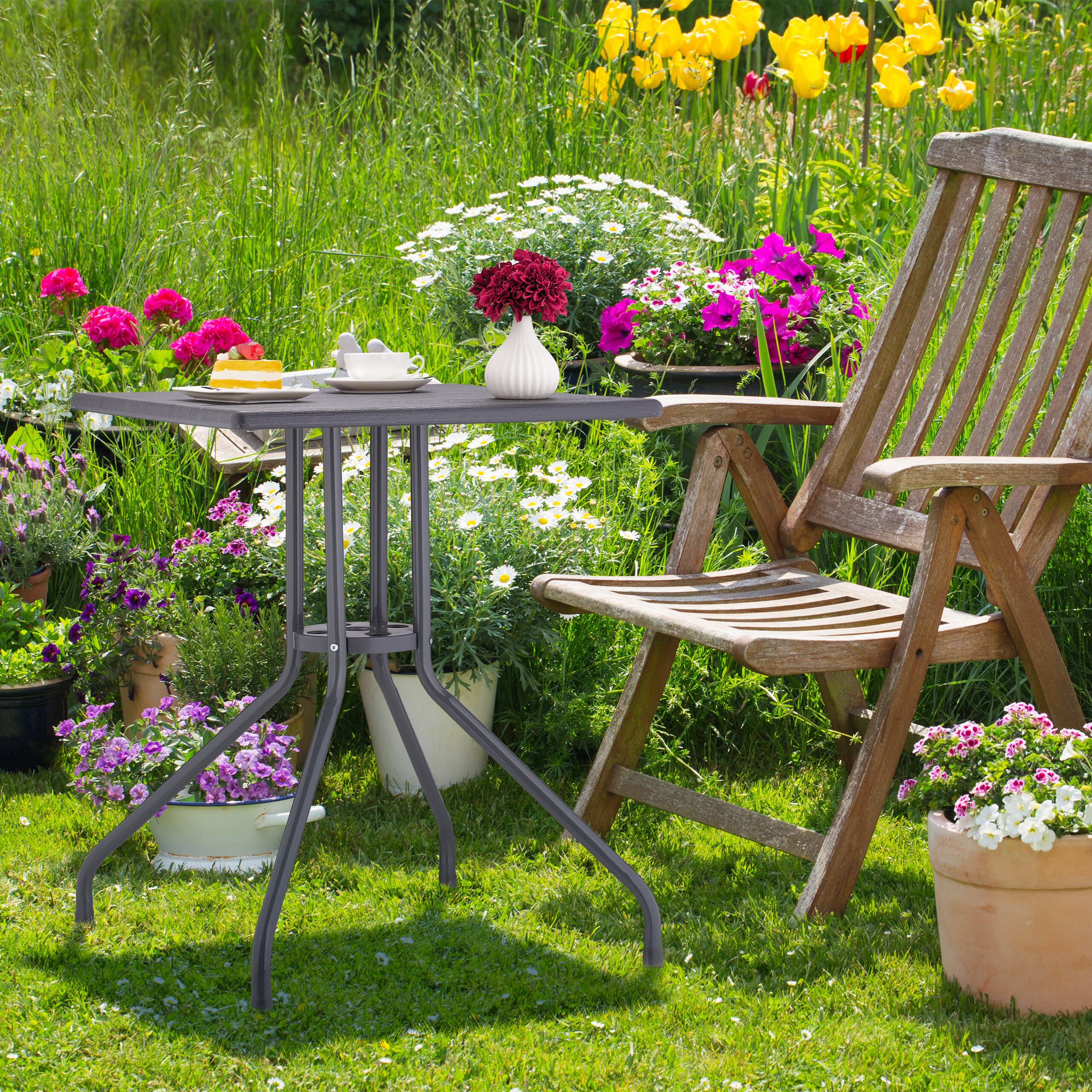 Ein hölzerner Gartenstuhl und ein kleiner Metalltisch mit Kuchen und Kaffee stehen im Garten.