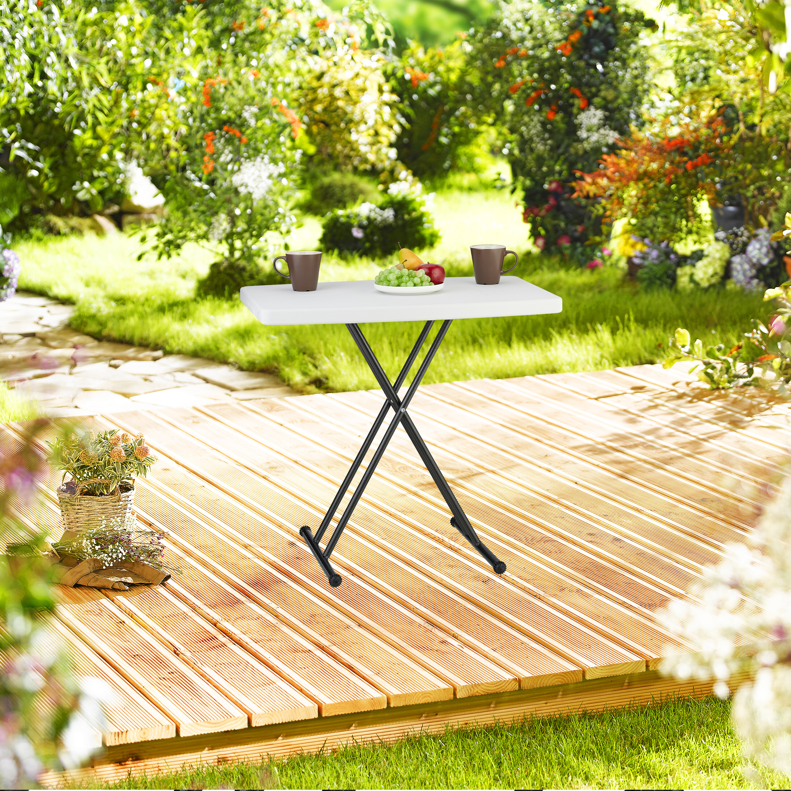 Ein kleiner weißer Klapptisch mit zwei Tassen und Obst steht auf einer Holzterrasse in einem Garten.