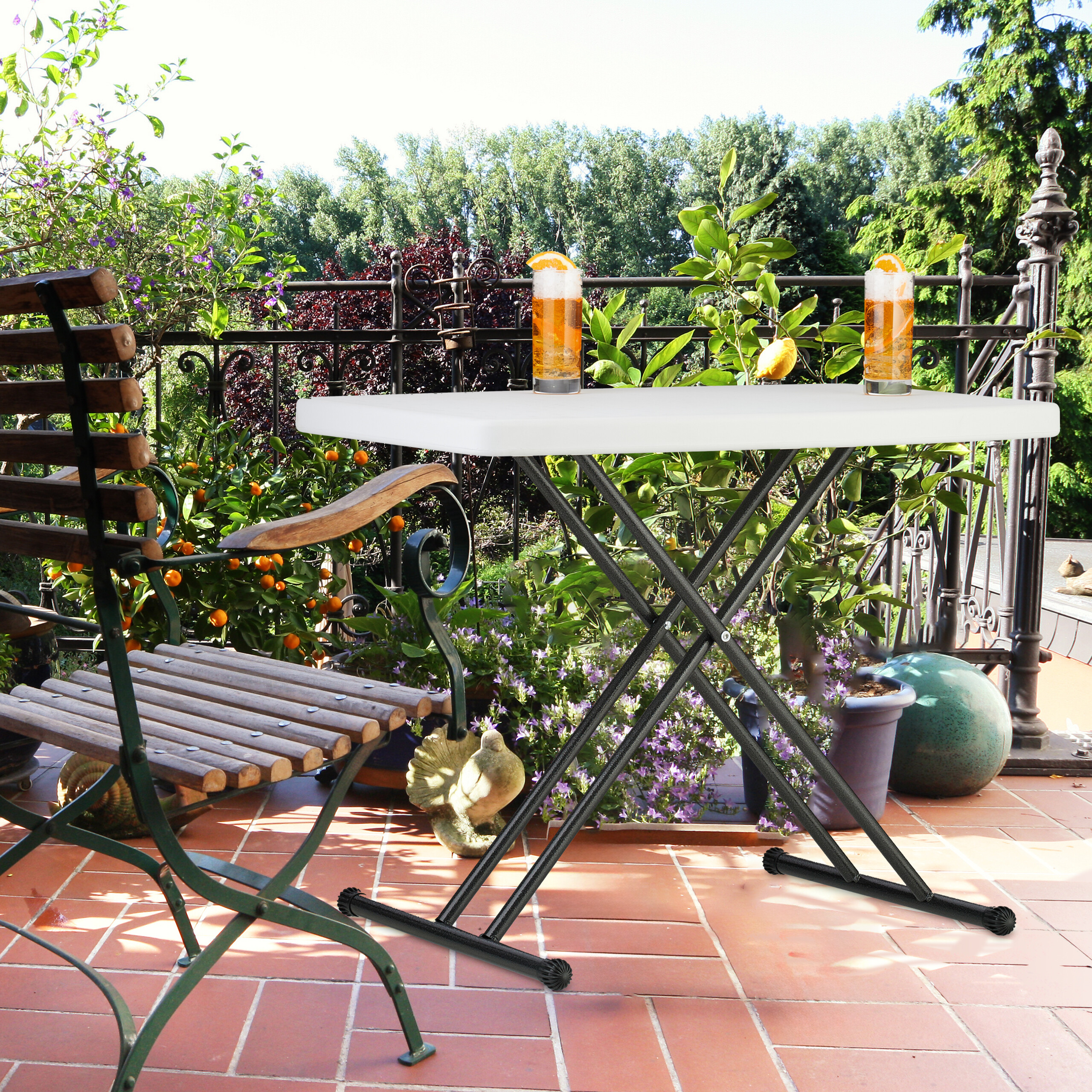Ein weißer Klapptisch mit zwei Getränken steht auf einer sonnigen Terrasse neben einem Holzsessel und Pflanzen.