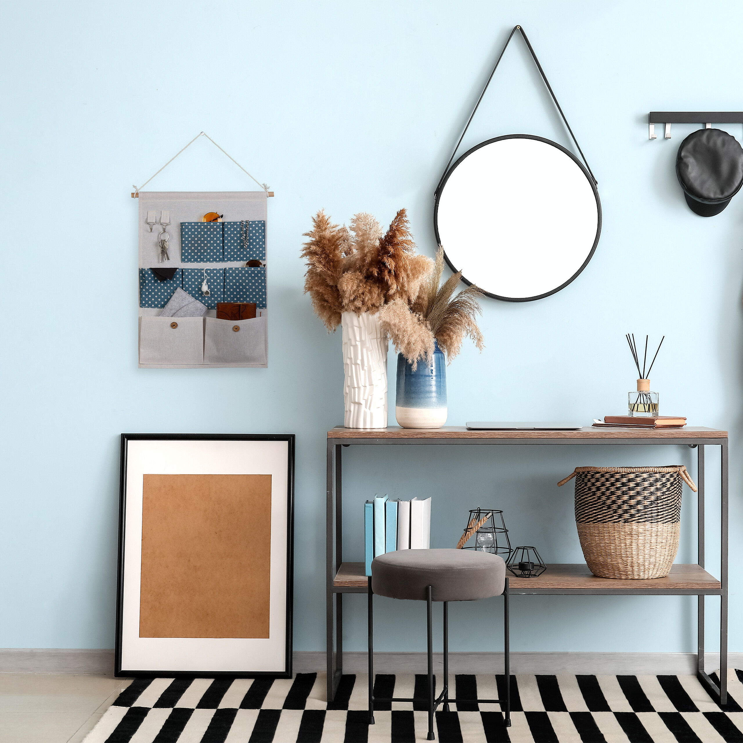 Ein heller Raum mit Konsole, rundem Spiegel, gerahmtem Bild, grauem Hocker und Wandorganizer vor blauer Wand.