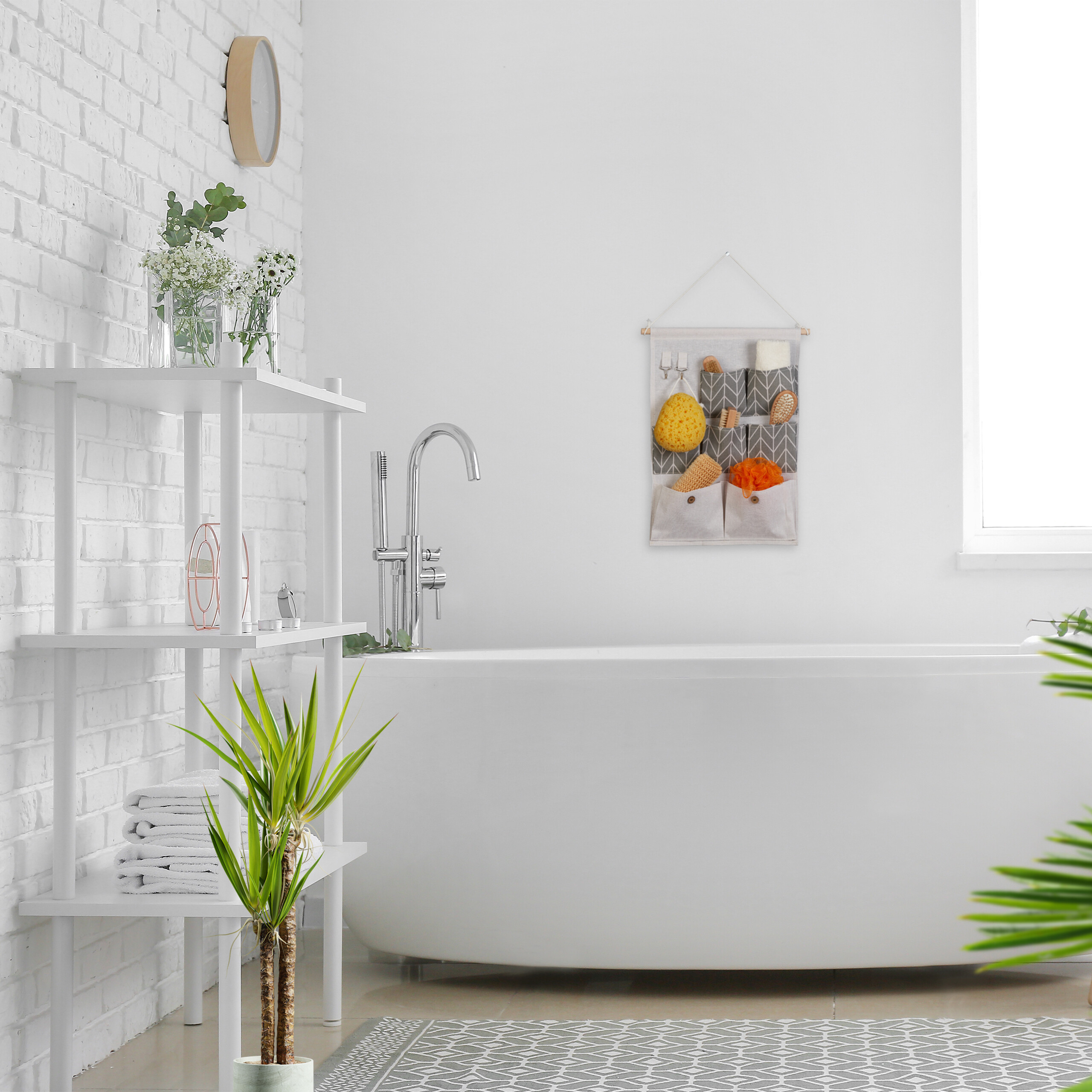Ein weißes Badezimmer mit Badewanne, Hängeorganizer, weißem Regal mit Handtüchern und Pflanzen sowie gemustertem Teppich.