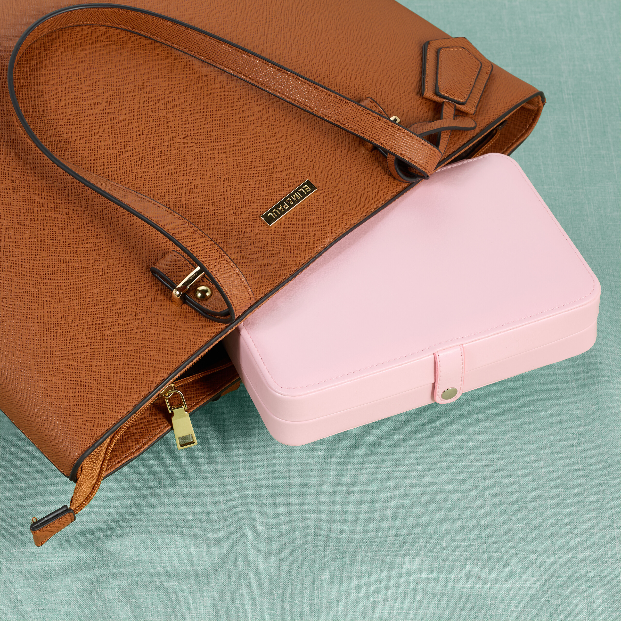 Eine braune Handtasche mit einer rosa Schmuckschatulle darin auf einer türkisen Oberfläche.