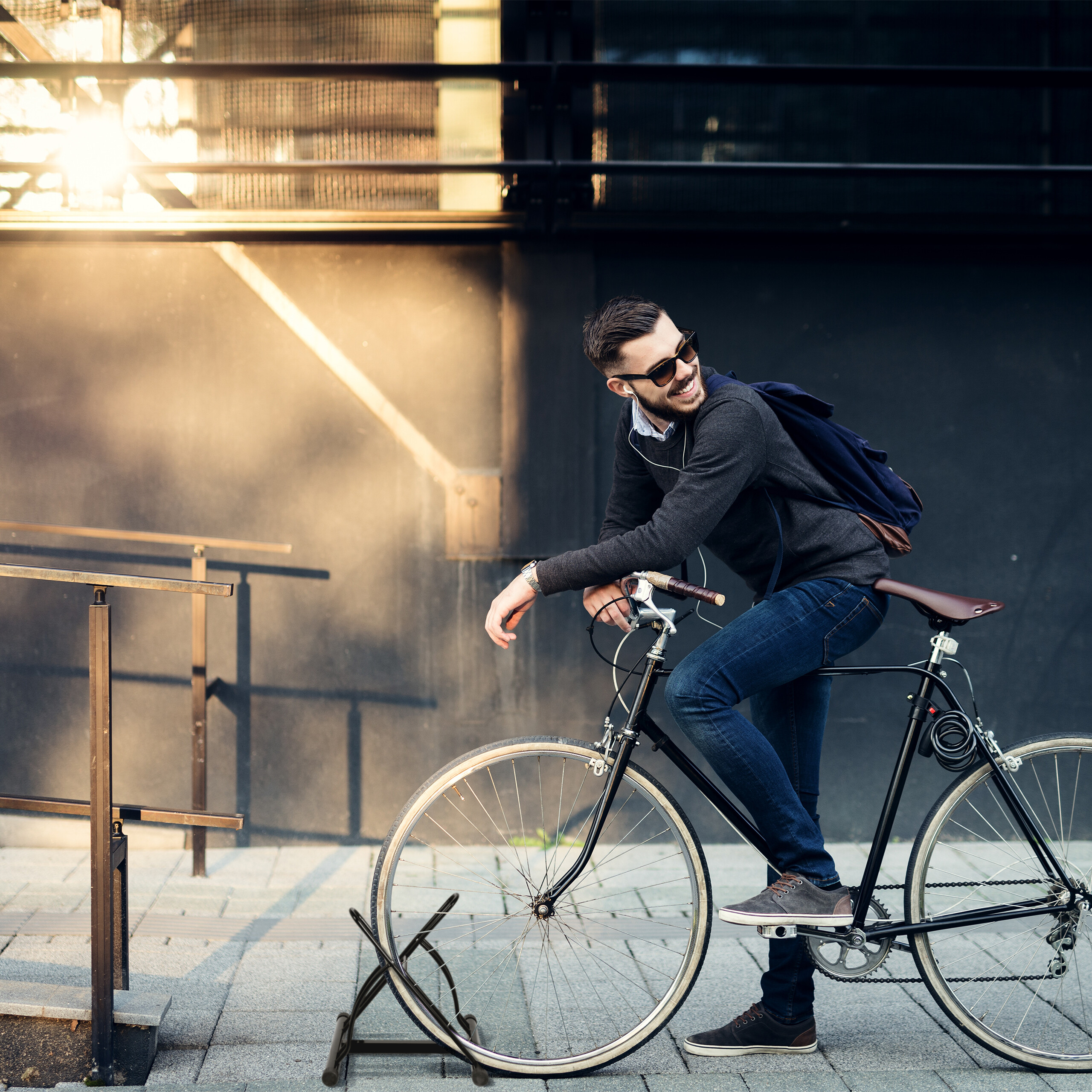 Ein lächelnder Mann mit Sonnenbrille sitzt vor einer dunklen Wand auf einem Fahrrad.