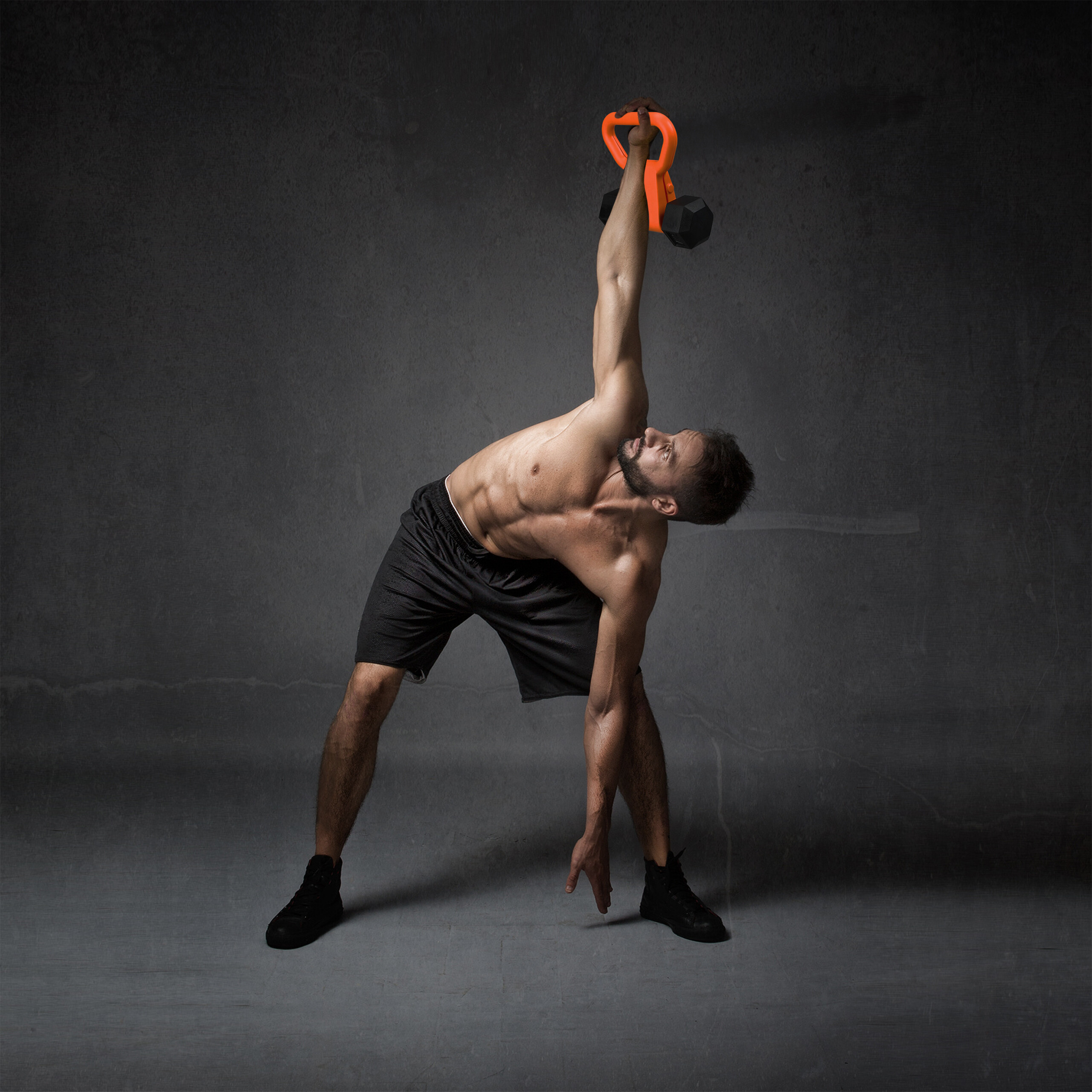 Ein muskulöser Mann in schwarzen Shorts hebt vor dunklem Hintergrund eine orangefarbene Kettlebell.