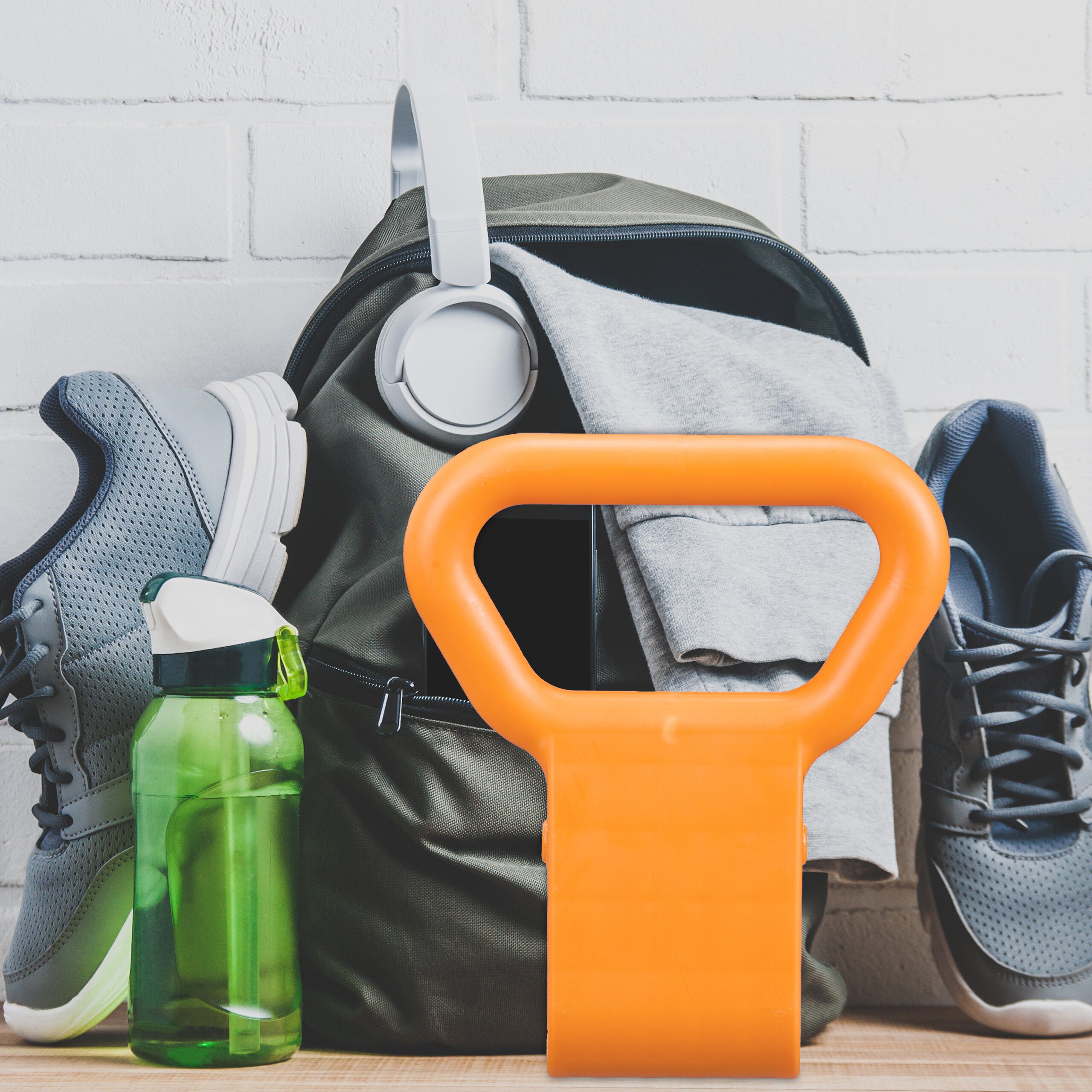 Ein grüner Rucksack mit Kopfhörern, Sportflasche, grauen Sneakers und einer orangefarbenen Kettlebell davor.